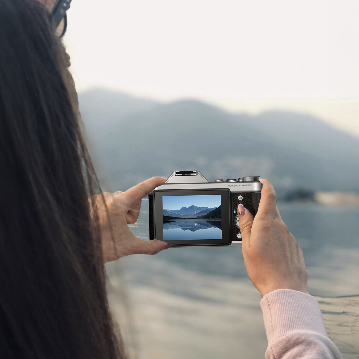Osoba trzymająca aparat, robiąca zdjęcie gór odbijających się w wodzie. Aparat wyświetla obraz na ekranie.