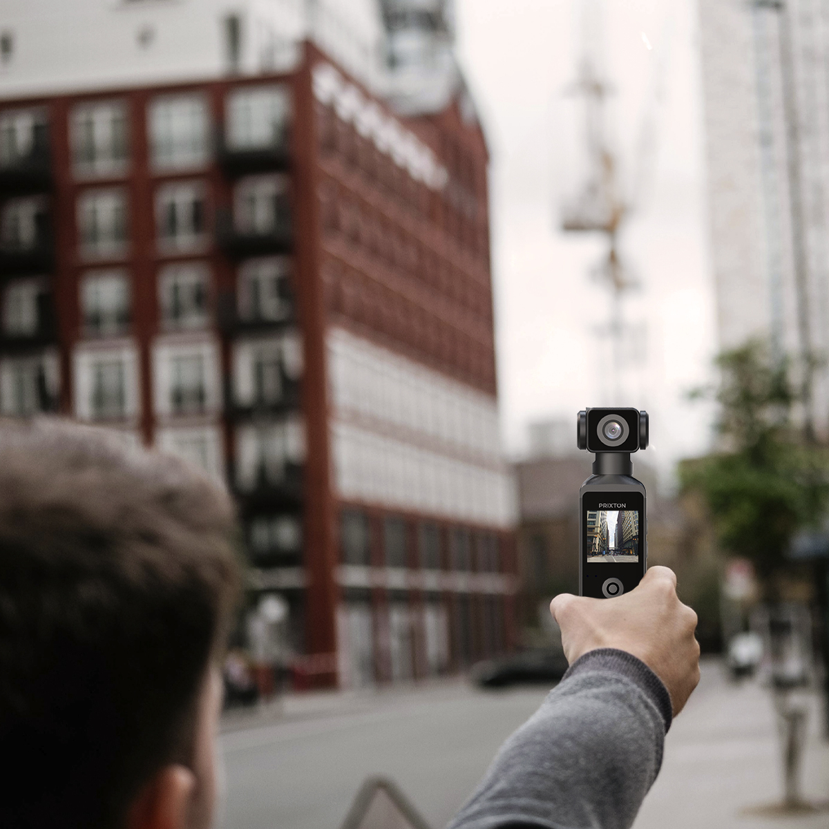 Osoba trzymająca czarną kamerę filmuje scenę uliczną z budynkami. Ekran kamery pokazuje podobny widok.