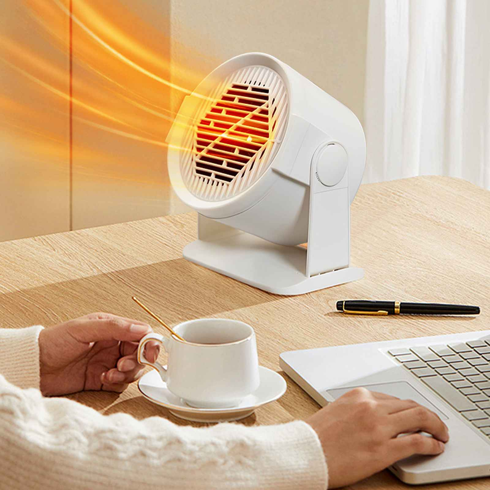 Ein weißer Heizlüfter mit orangefarbener Luftströmung steht auf einem Schreibtisch. Eine Tasse Tee, ein Laptop und ein Stift liegen ebenfalls auf dem Schreibtisch.