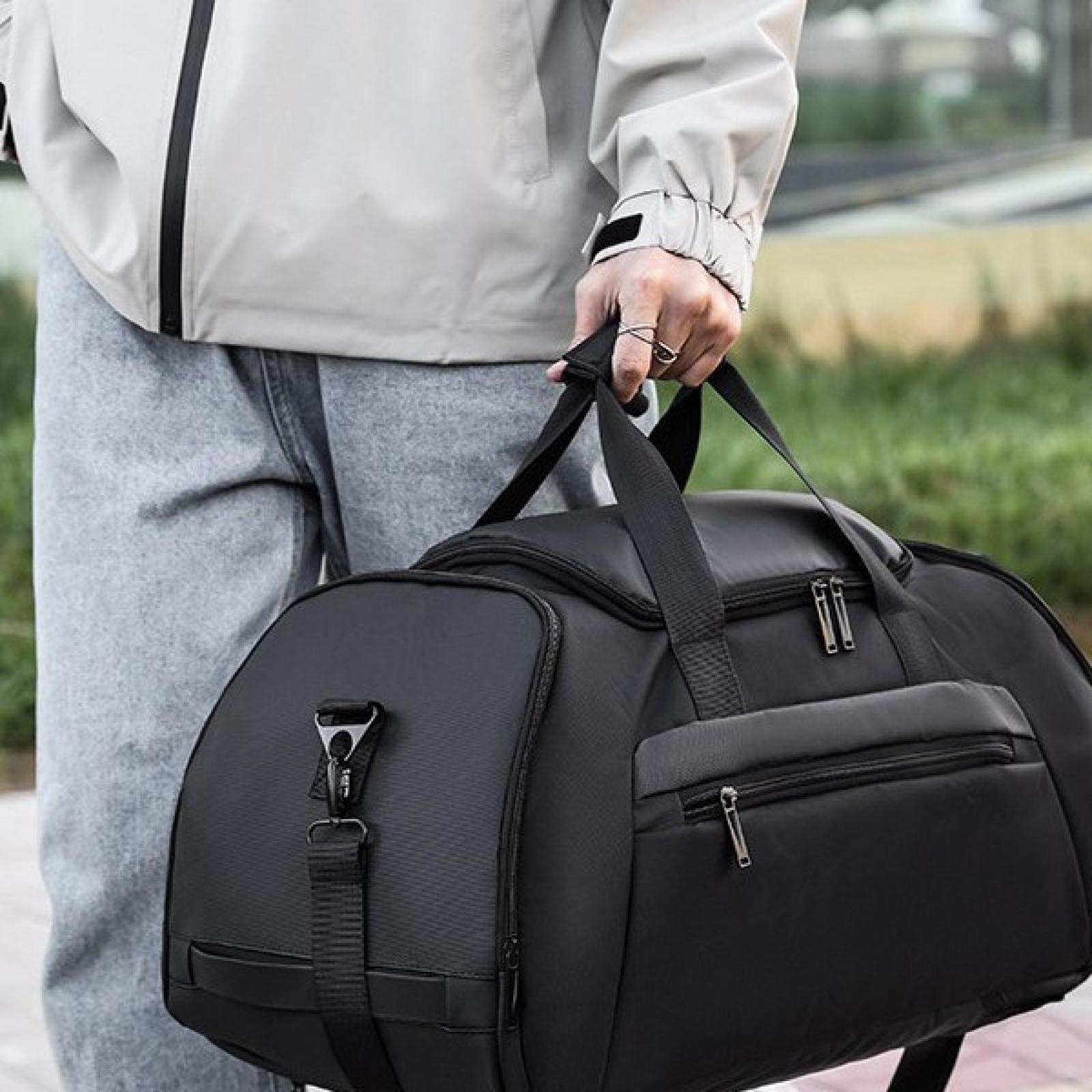 Eine Person hält eine schwarze Reisetasche mit Reißverschluss. Die Person trägt eine helle Jacke und graue Hose. Grüner Hintergrund.