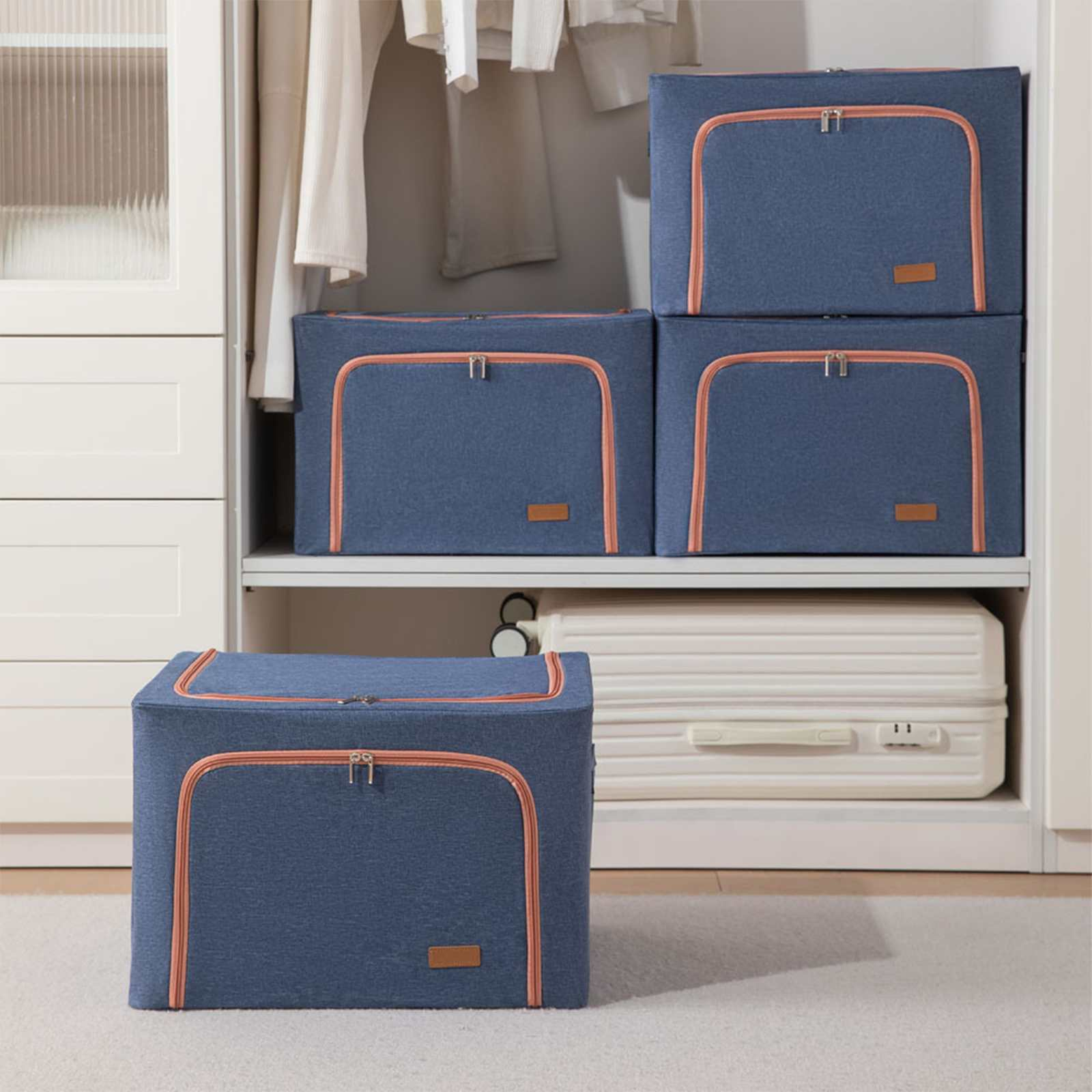 Blaue Aufbewahrungsboxen mit orangefarbenen Zierleisten in einem Schrank, eine auf dem Boden. Weißer Koffer und Kleidung im Hintergrund.