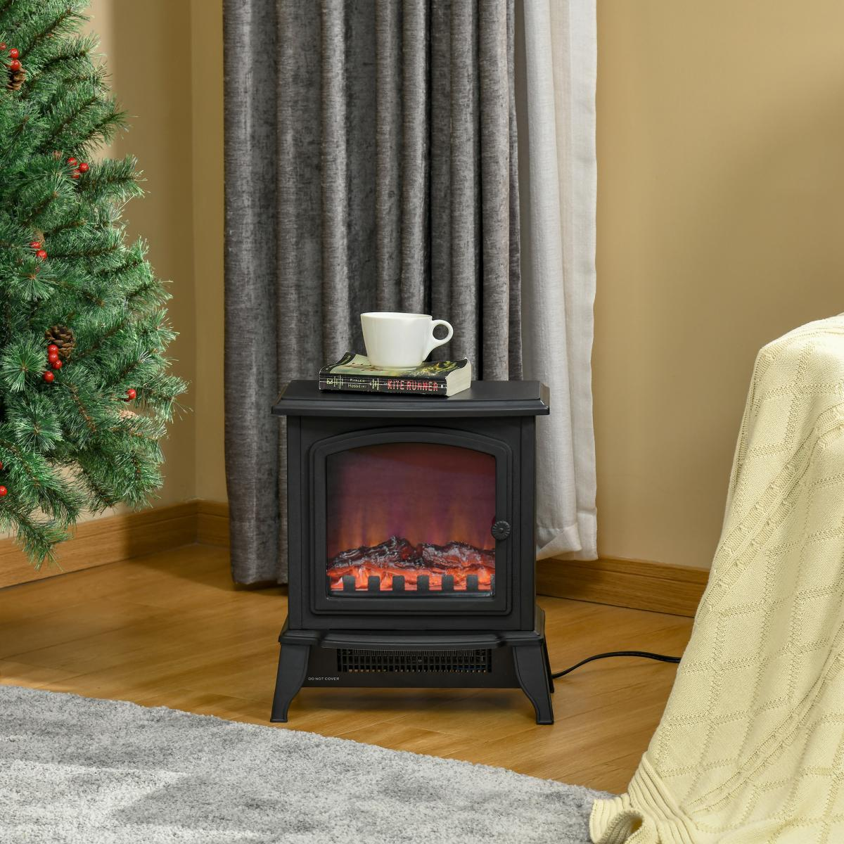Schwarzer elektrischer Kamin mit Tasse und Buch. Ein Weihnachtsbaum steht links. Eine Decke ist rechts.