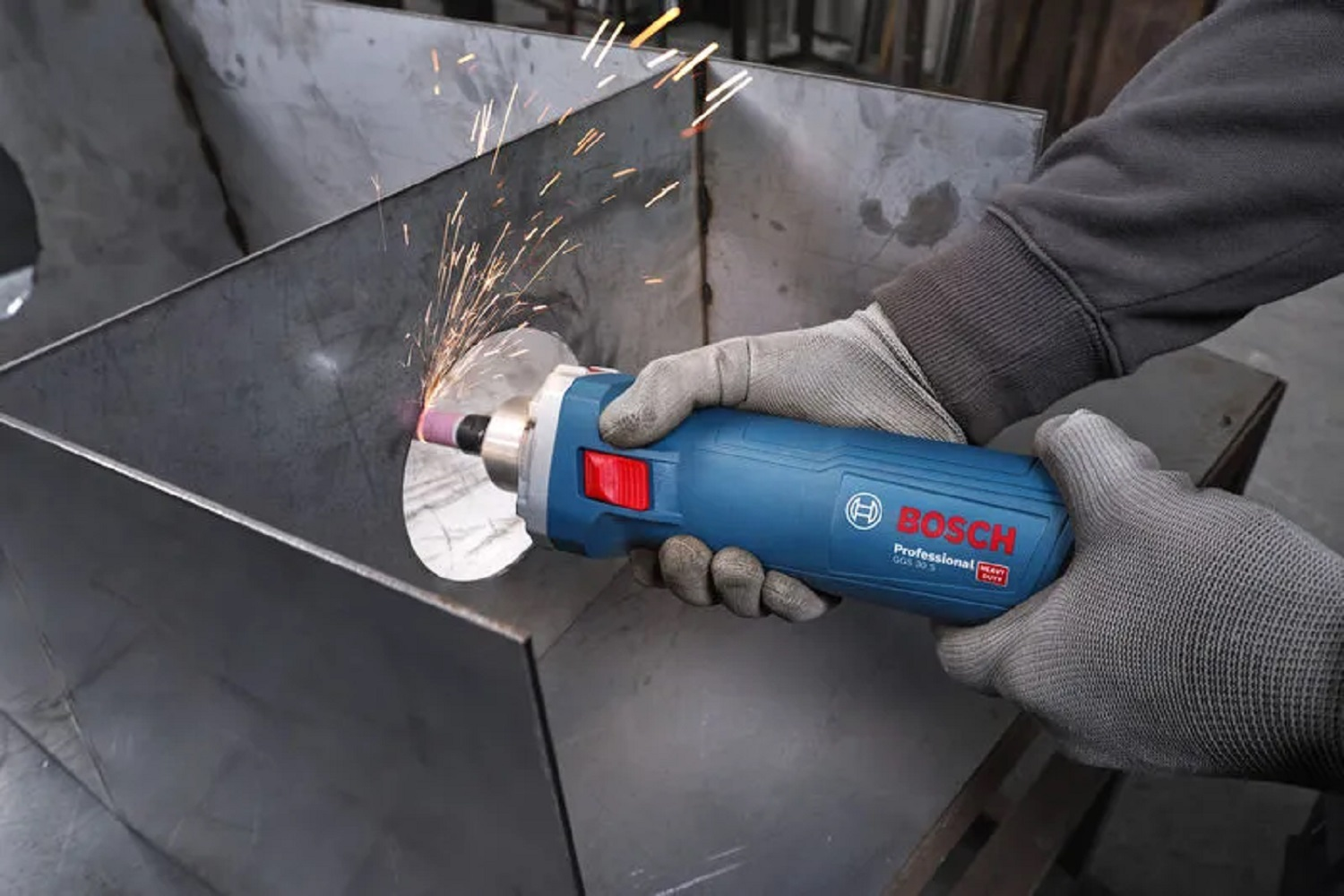 Ein Arbeiter schleift Metall mit einem Bosch-Werkzeug. Funken fliegen. Das Werkzeug ist blau und schwarz. Der Arbeiter trägt graue Handschuhe.