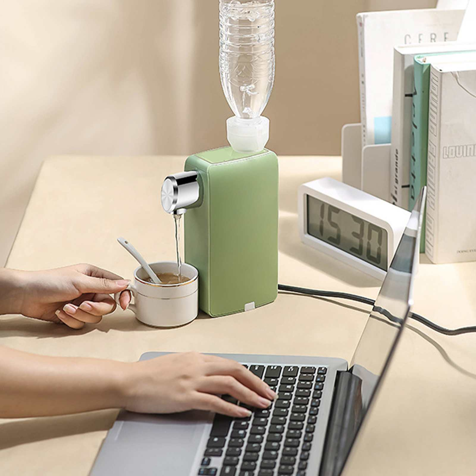 Eine Person arbeitet an einem Laptop, mit einem kleinen Wasserspender, einer Tasse Tee und Büchern auf dem Schreibtisch.