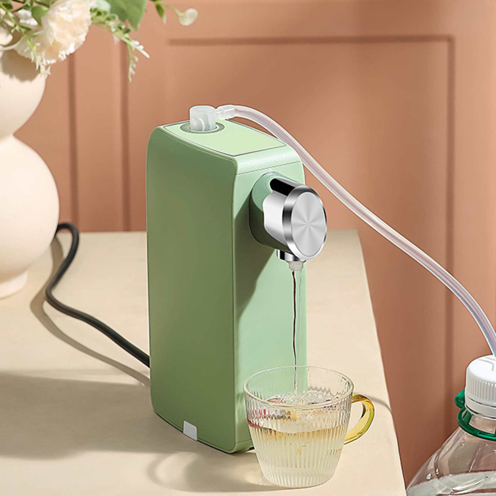 Ein grüner Wasserspender steht auf einem Tisch. Wasser fließt in ein Glas. Eine weiße Vase und eine Wasserflasche sind zu sehen.