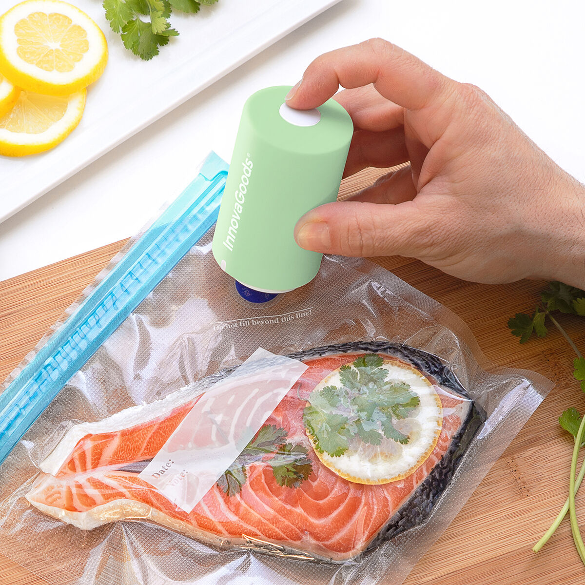 Una mano preme una sigillatrice sottovuoto verde su un sacchetto con salmone e fette di limone. Coriandolo e fette di limone sono anche sulla tavola.