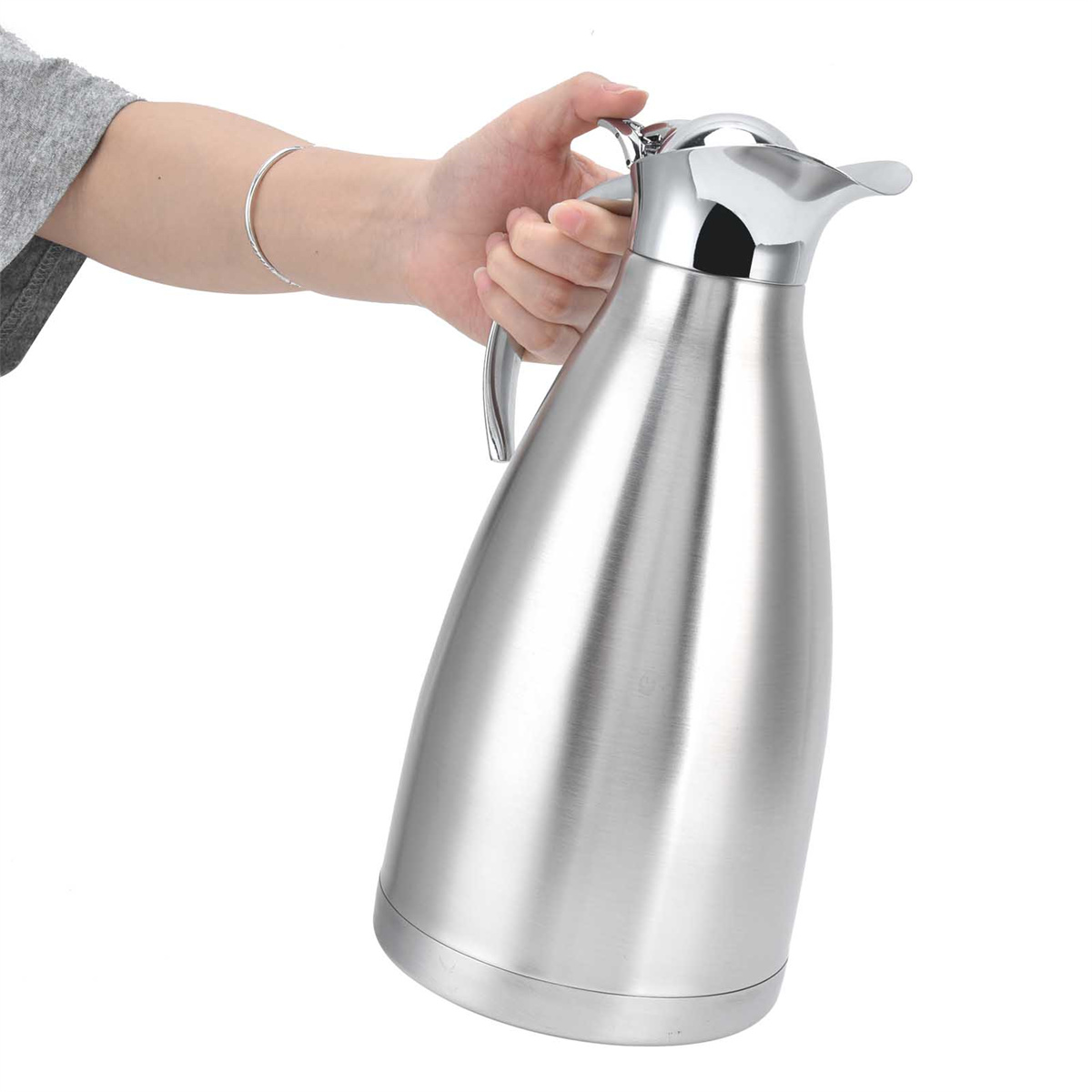 Eine Hand hält eine silberne Edelstahl-Thermoskanne. Die Kanne hat einen Griff und einen Ausguss. Der Hintergrund ist weiß.