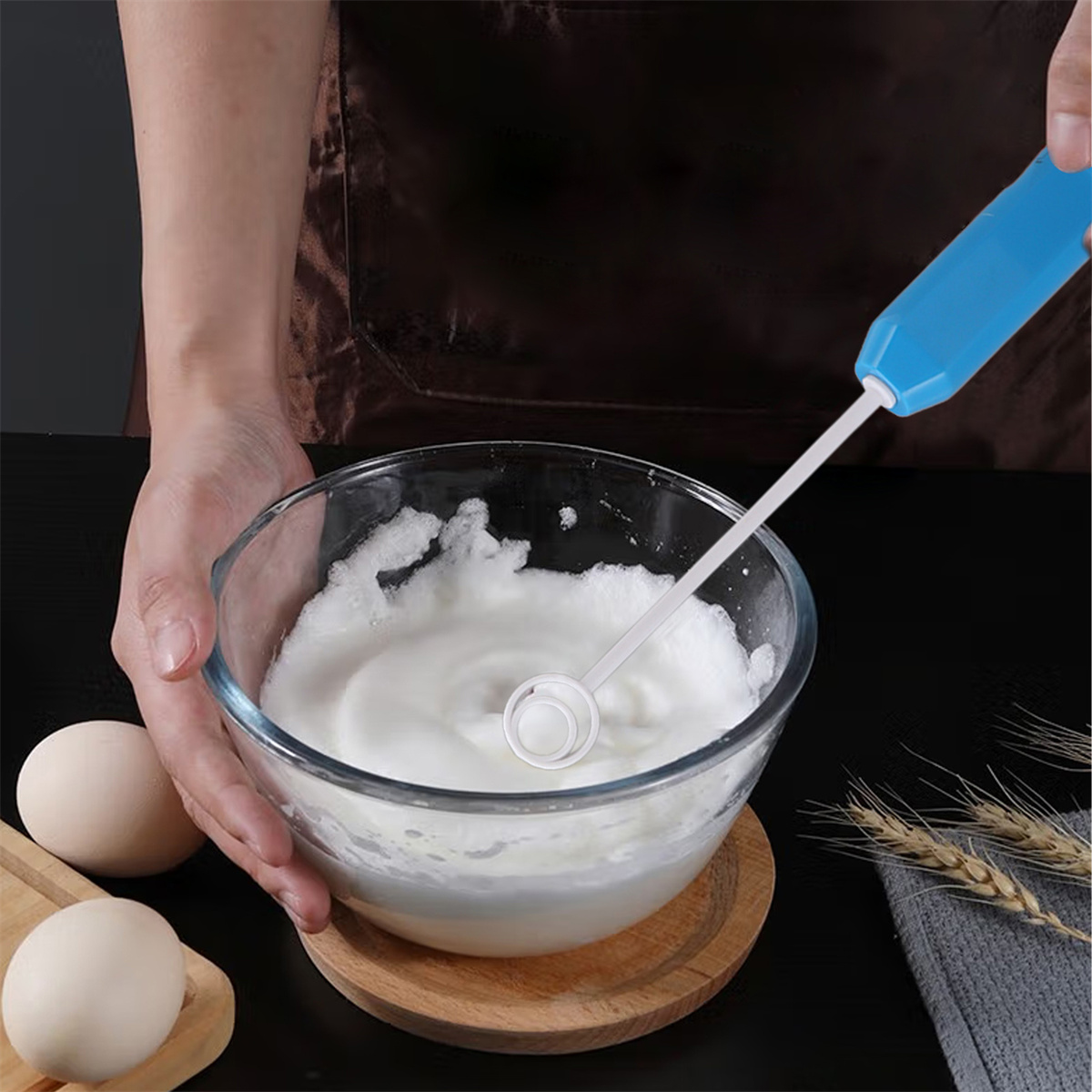 Eine Person schlägt Eischnee mit einem elektrischen Mixer in einer Glasschüssel. Zwei Eier liegen auf einem Holzbrett.