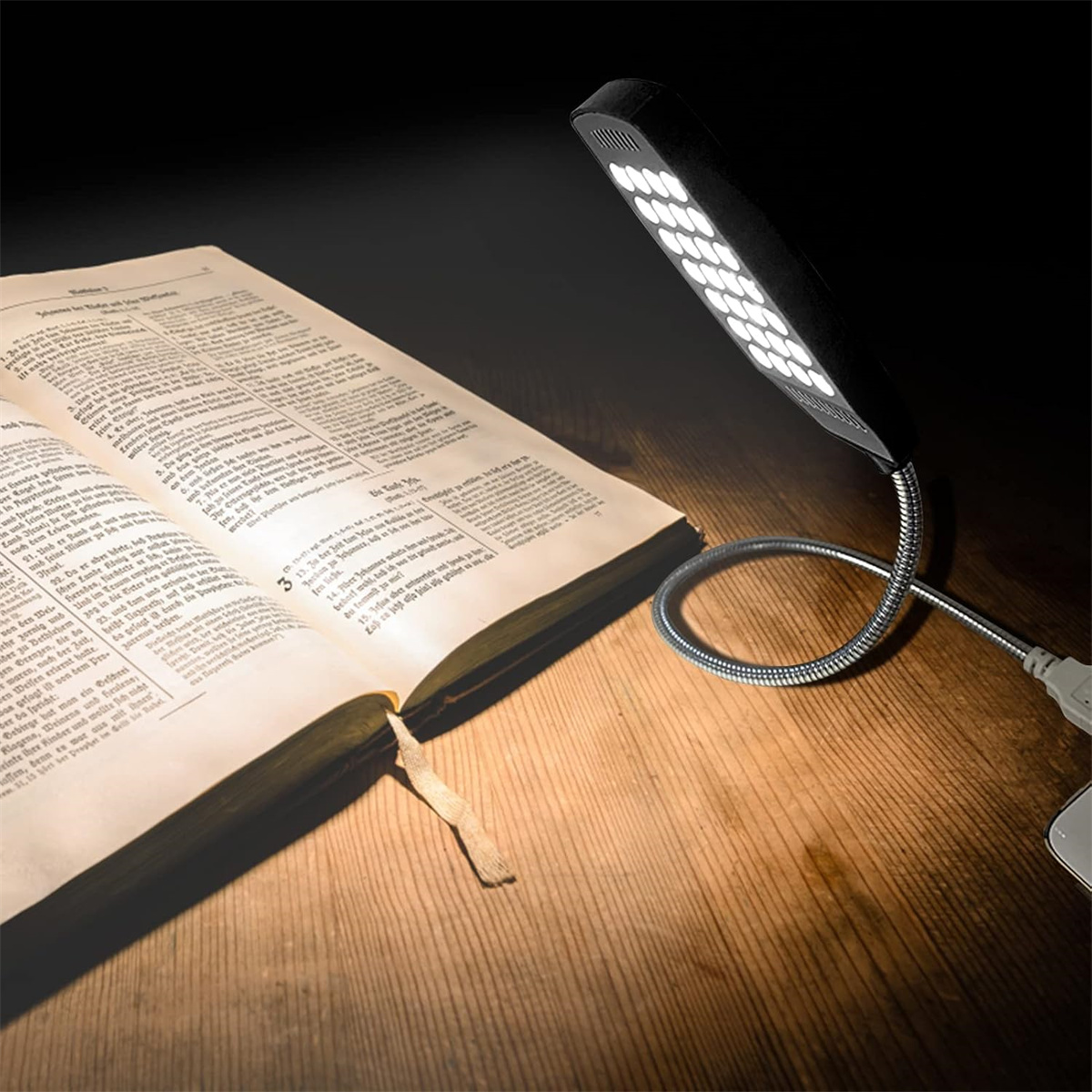 Eine schwarze LED-Buchleuchte beleuchtet ein offenes Buch auf einem Holztisch. Das Buch hat ein Lesezeichen.