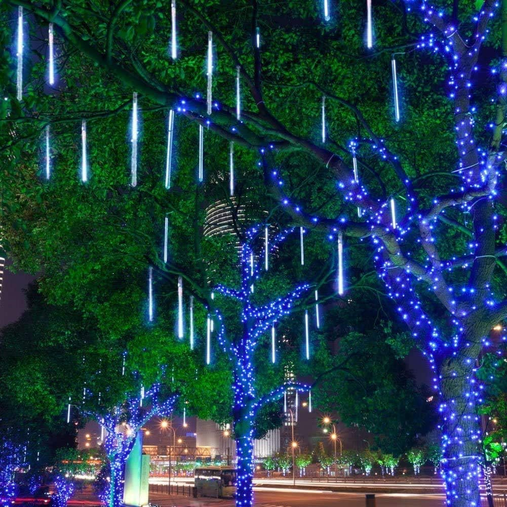 Bäume mit blauen Lichtern und fallenden Eiszapfenlichtern geschmückt, Stadtgebäude im Hintergrund, Nachtszene.