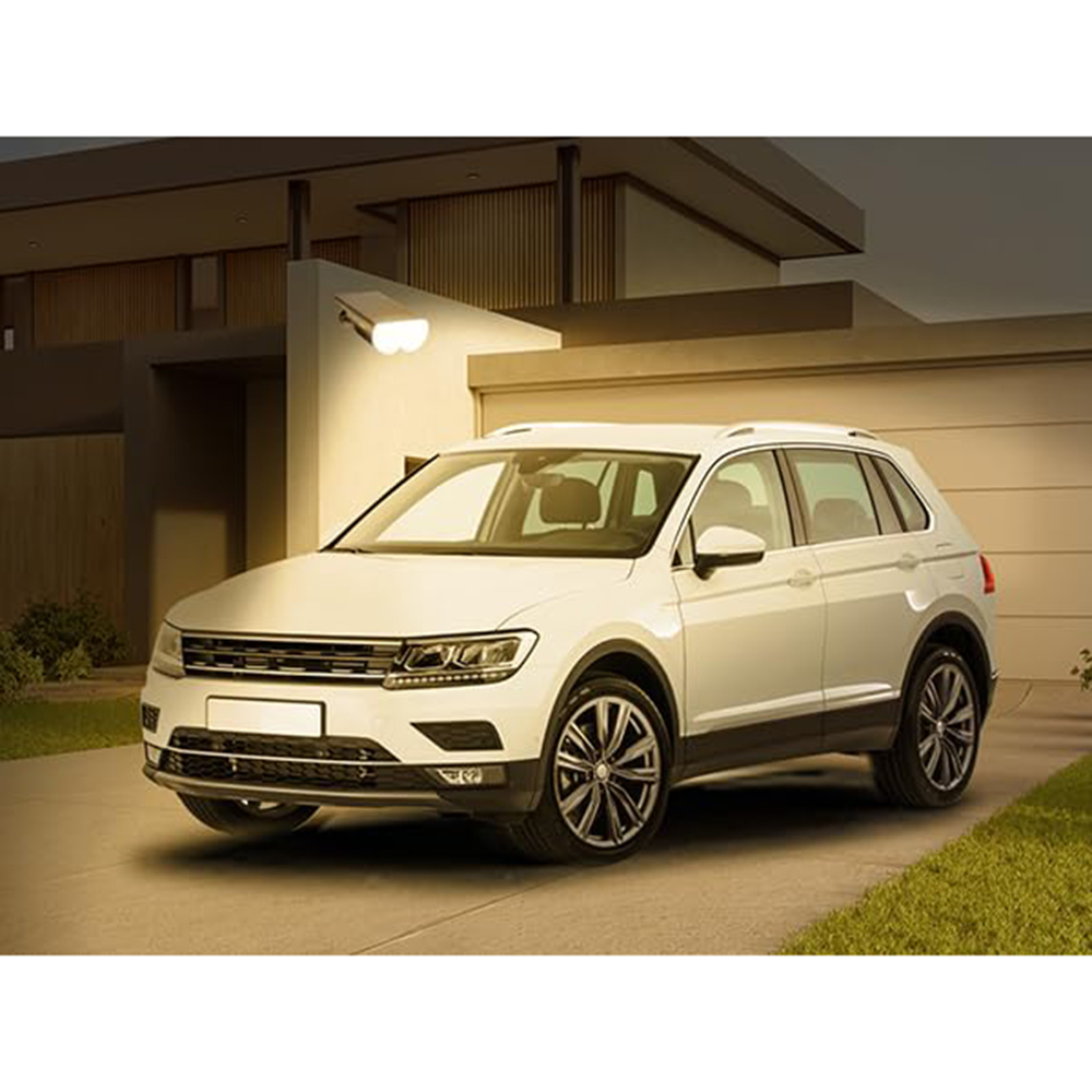 Ein weißer SUV steht vor einem Haus. Ein Scheinwerfer beleuchtet das Auto und einen Teil des Hauses. Die Szene ist nachts beleuchtet.