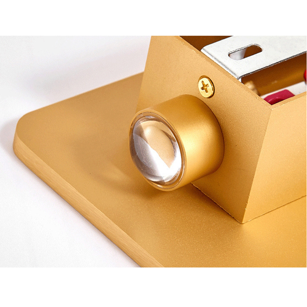 Detail einer goldenen Lampe mit klarer Linse, Schraube und Metallelement, alles auf goldenem Sockel, vor weißem Hintergrund.