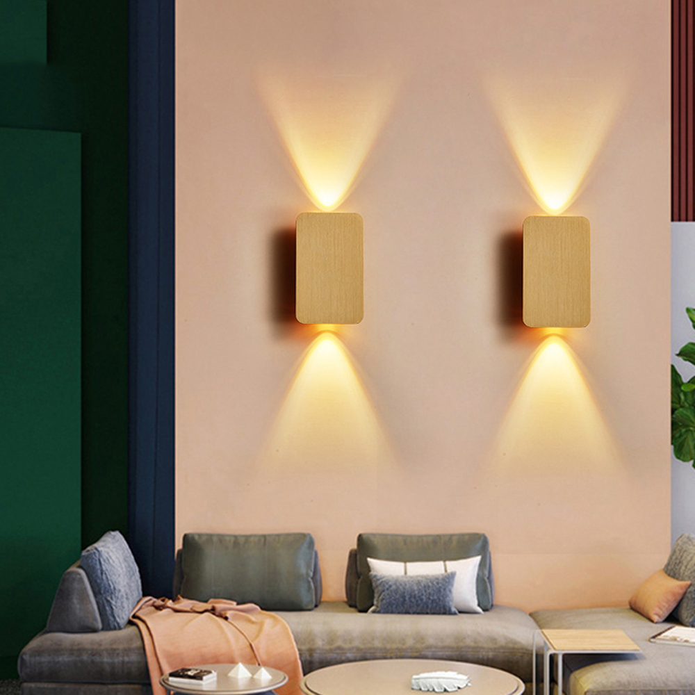 Zwei Wandlampen aus Holz leuchten nach oben und unten auf einer rosa Wand. Darunter befinden sich zwei Sofas und ein Tisch.