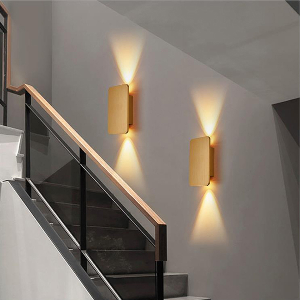 Treppe mit Holzhandlauf, schwarzen Metallstützen und zwei Wandlampen, die die Stufen und die Wand beleuchten.