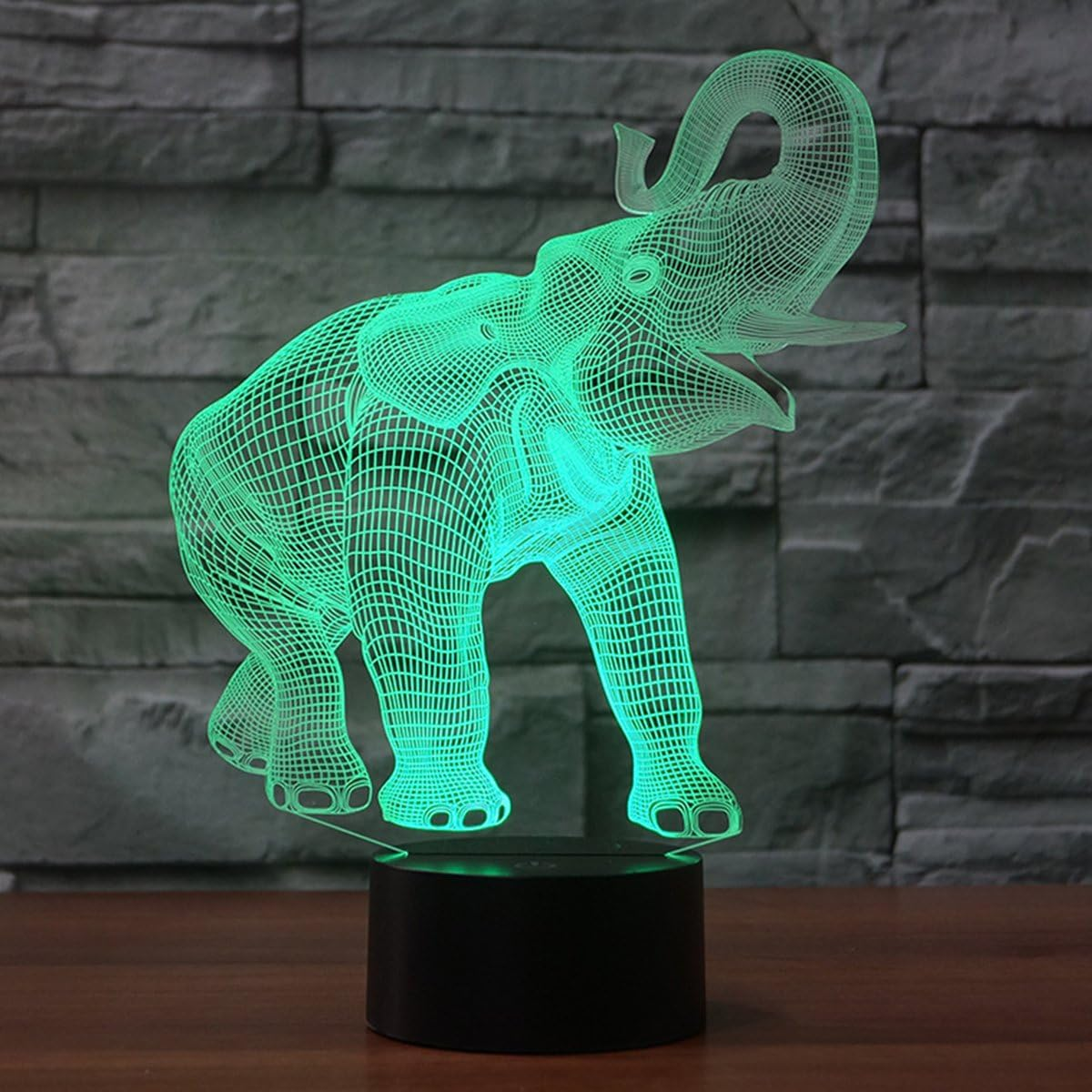 Eine 3D-Drahtgitter-Elefantenskulptur, die mit grünem Licht beleuchtet wird. Sie steht auf einem schwarzen Sockel vor einer grauen Steinmauer.