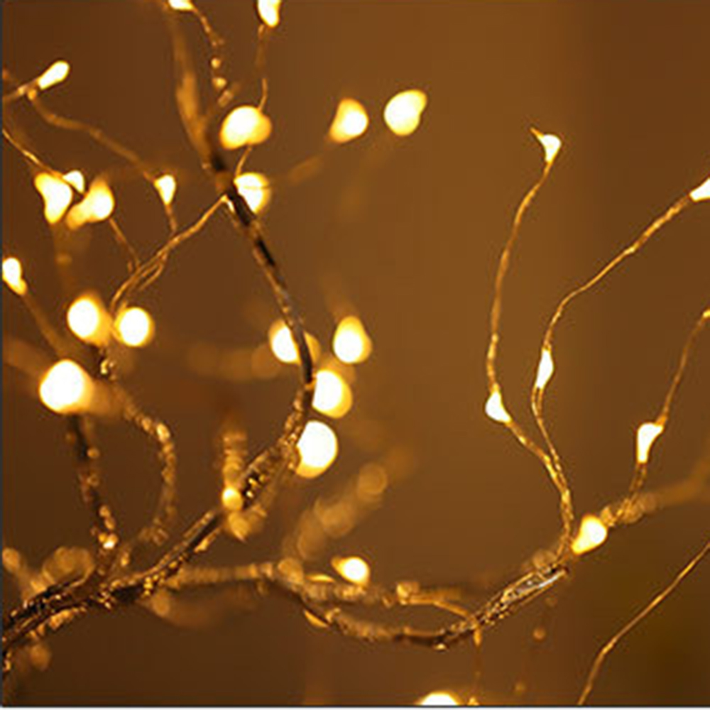 Nahaufnahme von warm leuchtenden Lichterketten an dünnen, sich windenden Ästen. Weichzeichner auf den Lichtern vor braunem Hintergrund.