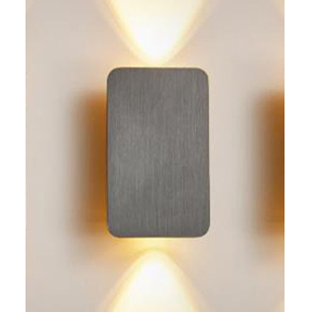Eine an der Wand befestigte Leuchte. Sie hat eine rechteckige, graue Metallfront. Licht scheint nach oben und unten und beleuchtet die beige Wand.