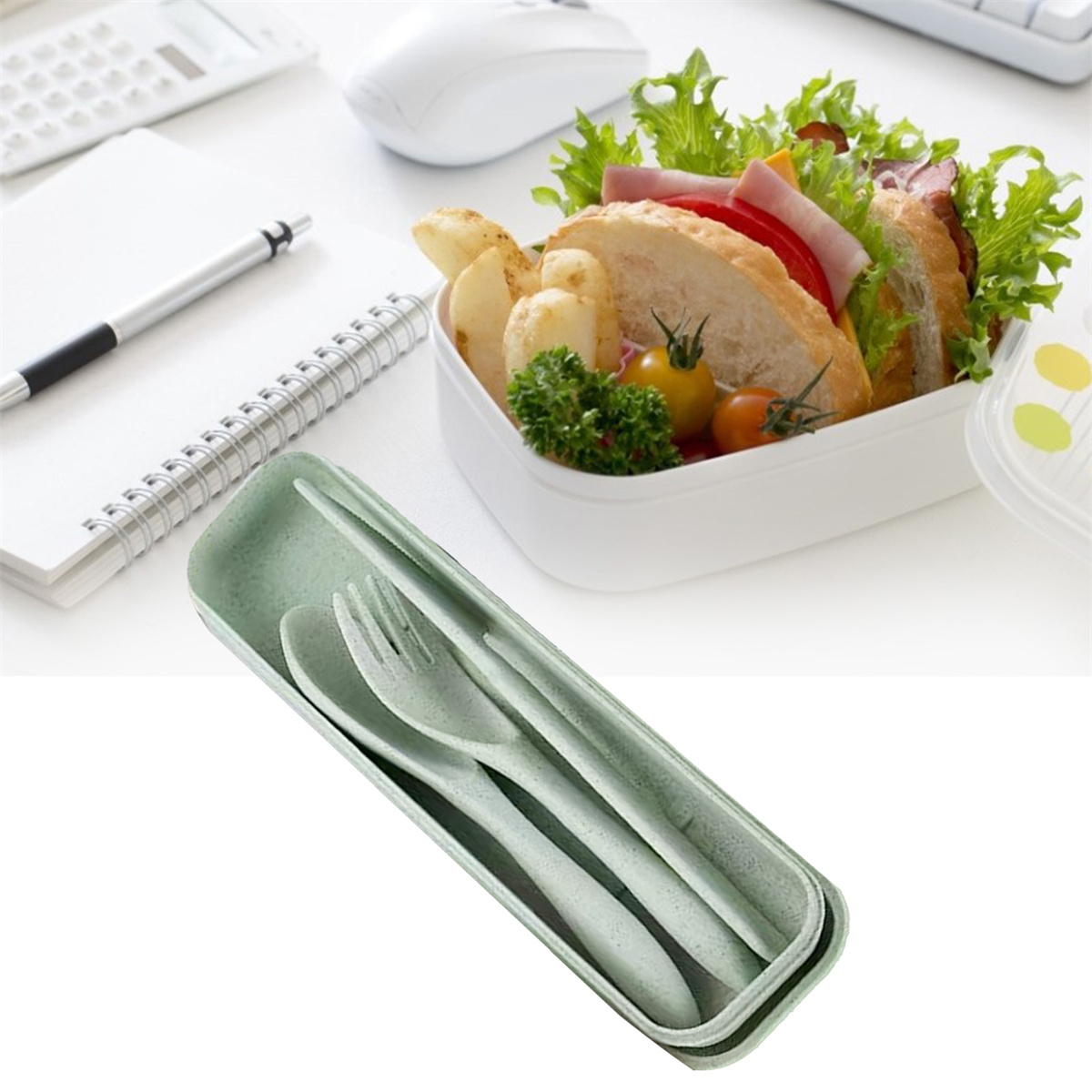 Eine Lunchbox mit Sandwich, Kartoffeln und Salat. Grünes Besteck in einer Hülle im Vordergrund. Notizbuch und Stift sichtbar.