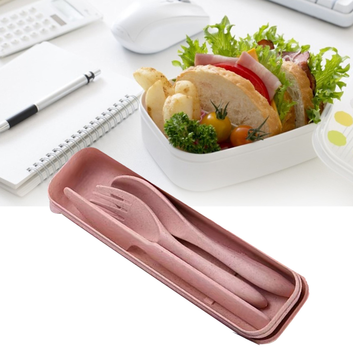 Lunchbox mit Sandwich, Tomaten und Salat. Rosa Besteckset davor. Notizbuch, Stift und Maus auf weißer Oberfläche.