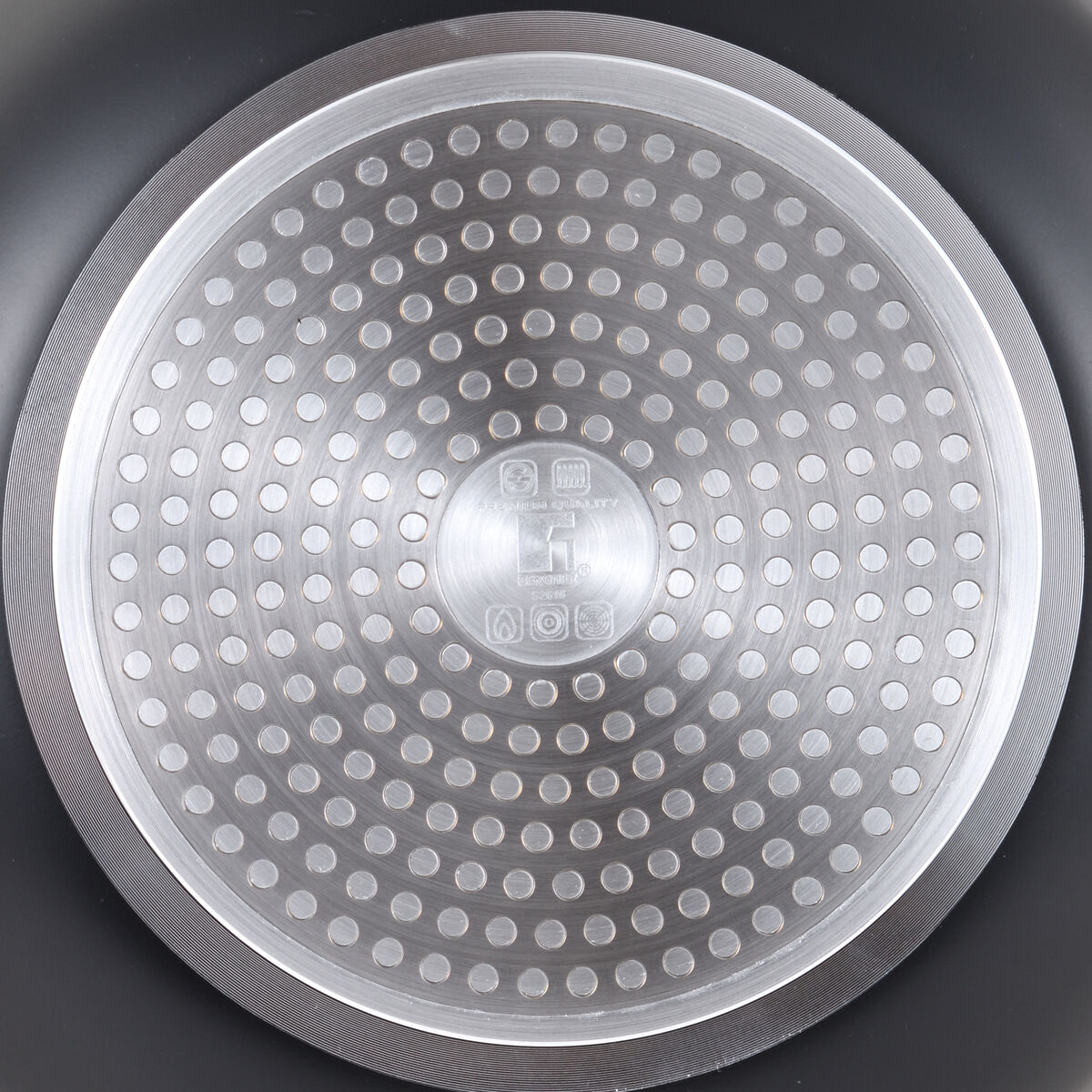 Nahaufnahme eines Pfannenbodens. Es hat ein kreisförmiges Design mit vielen kleinen Löchern. Ein metallischer Rand umgibt den Mittelbereich.