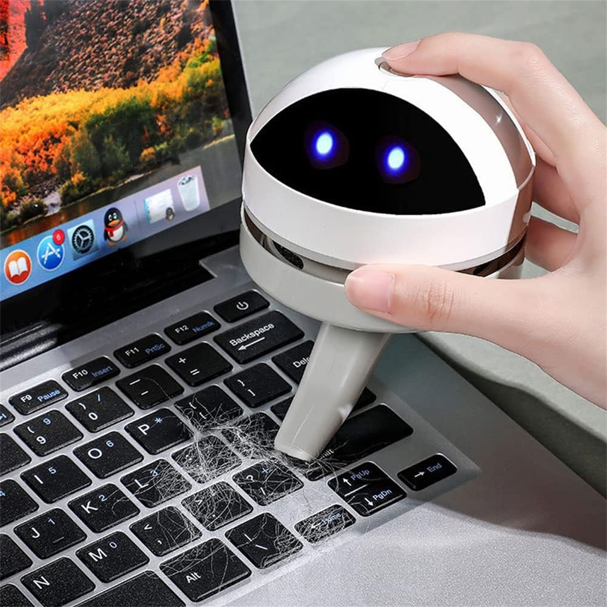 Ein kleiner Roboter-Staubsauger reinigt eine mit Staub und Schmutz bedeckte Laptop-Tastatur. Eine Hand drückt auf den Roboter.