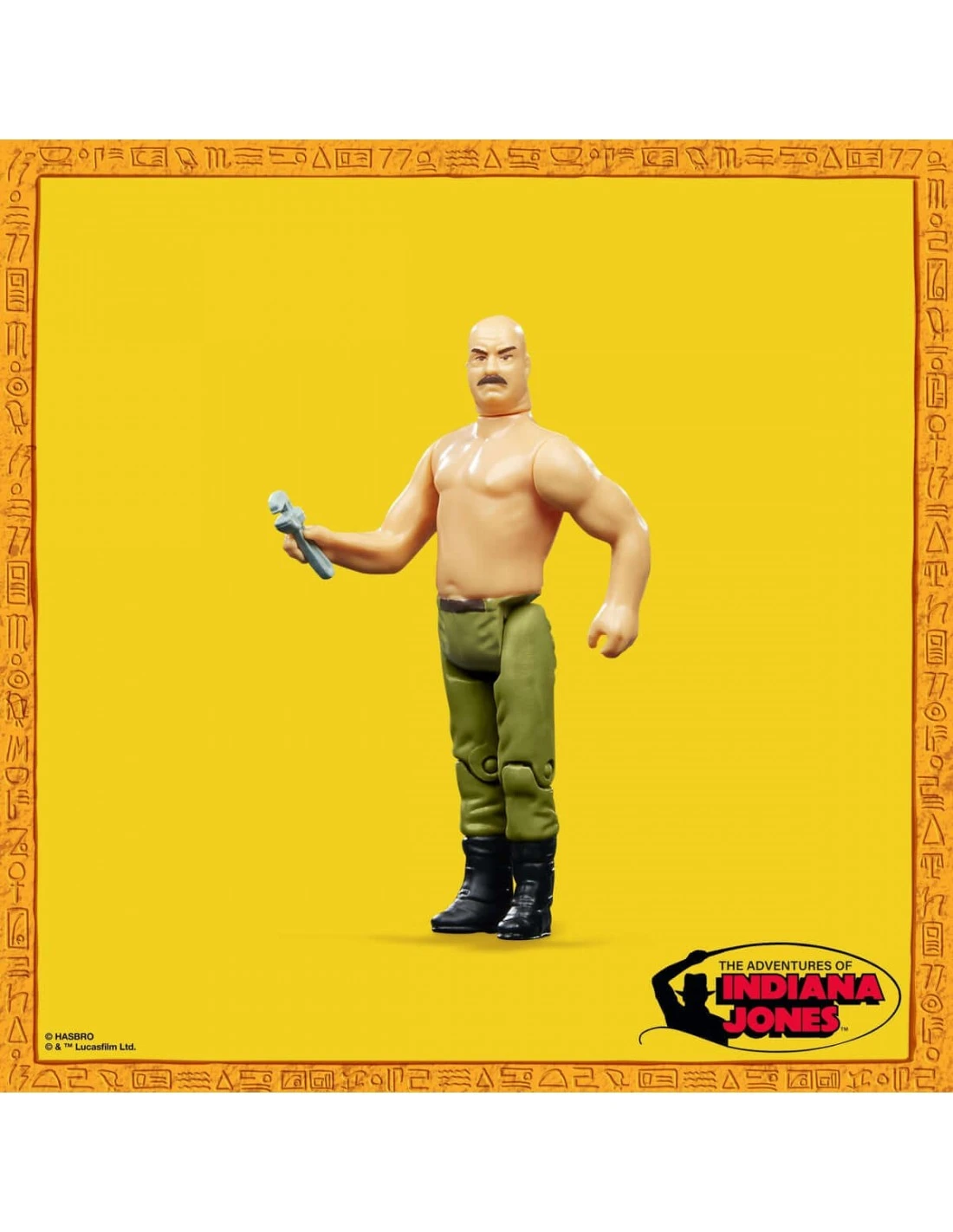 Figura de acción de un hombre calvo con bigote, sin camisa, con pantalones verdes y botas negras, sosteniendo una herramienta. Fondo amarillo.