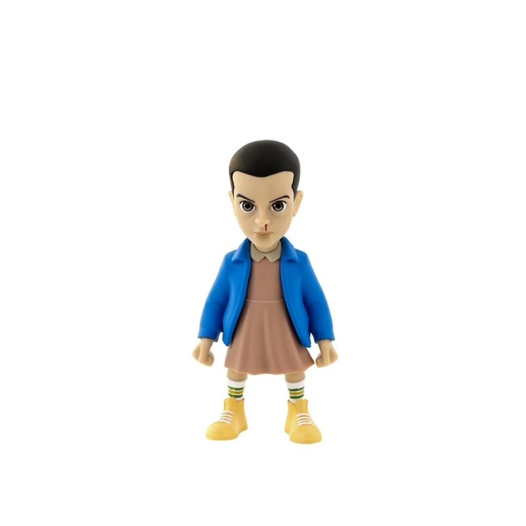 Una statuetta di Undici da Stranger Things, con giacca blu, vestito rosa e stivali gialli, su sfondo bianco.