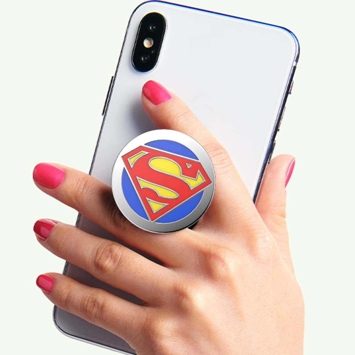 Una mano tiene un telefono con un supporto per telefono con il logo di Superman. Il logo è rosso e giallo su un cerchio blu. Le unghie sono dipinte di rosa.