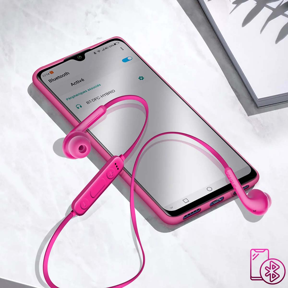Un telefono rosa mostra una connessione Bluetooth. Auricolari rosa collegati. Lo sfondo è una superficie bianca con ombra.