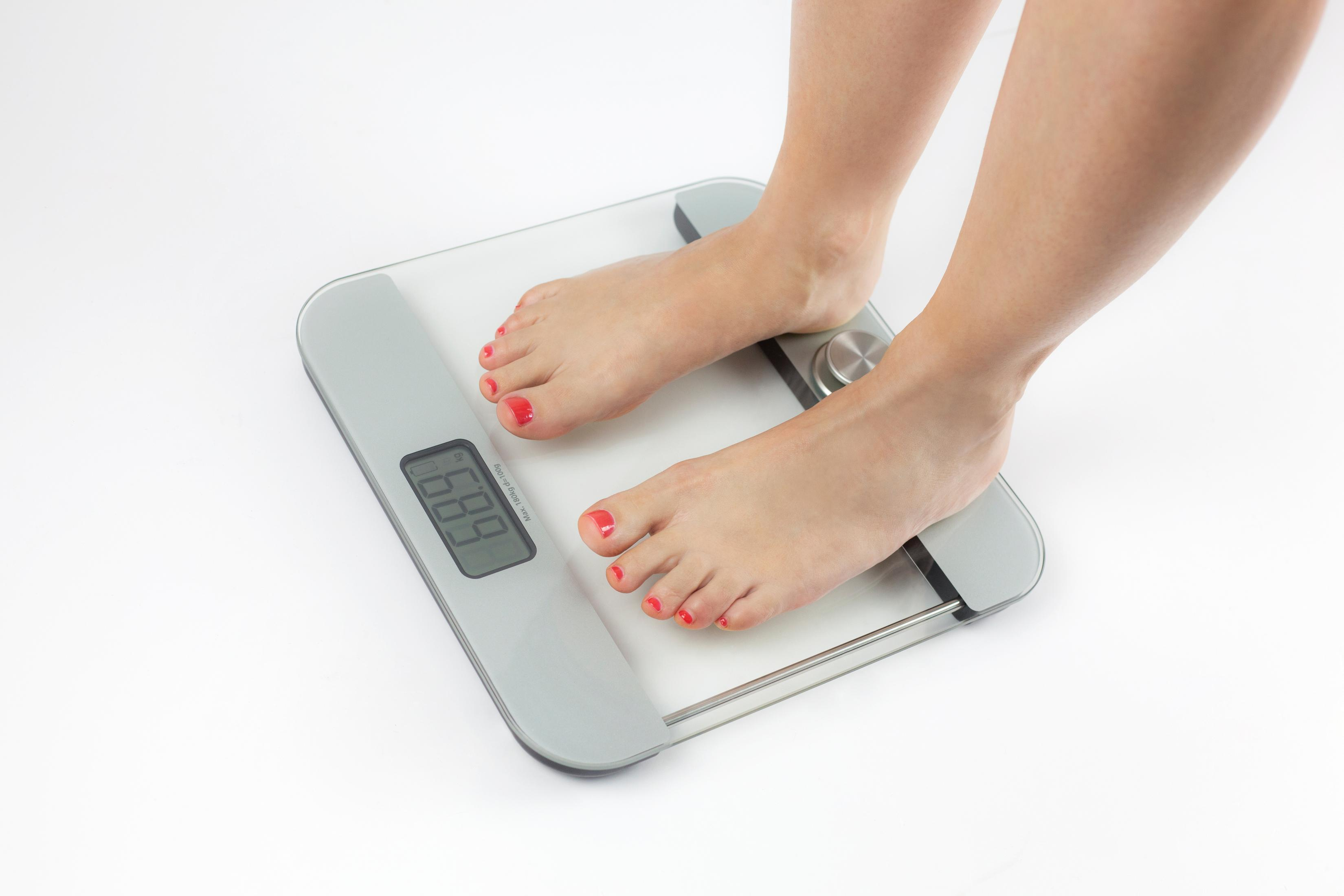Füße einer Person stehen auf einer Waage, die 68,9 kg anzeigt. Die Person hat roten Nagellack.