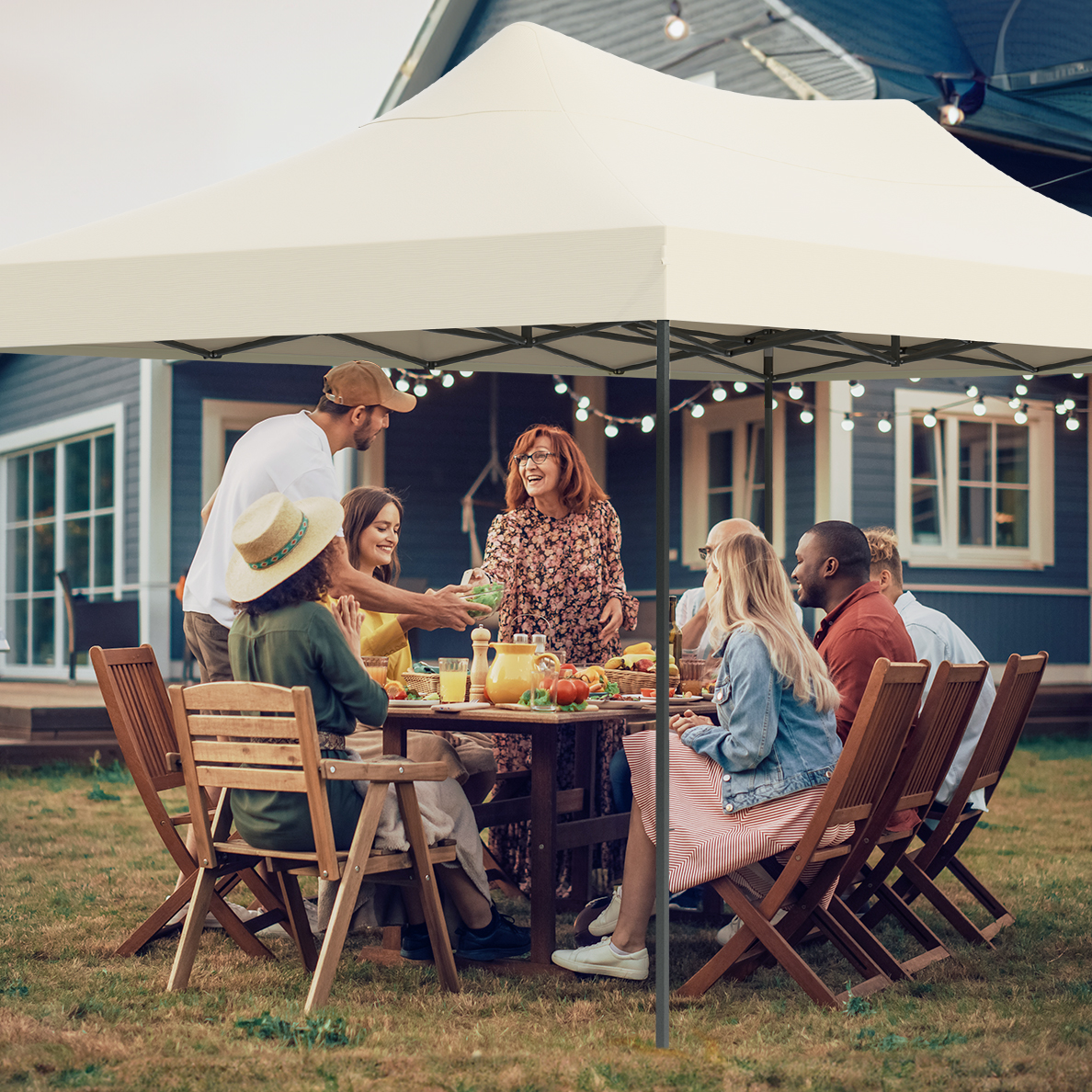 A group of people are sitting around a table under a tent, enjoying a meal. A man is passing a bowl of salad.