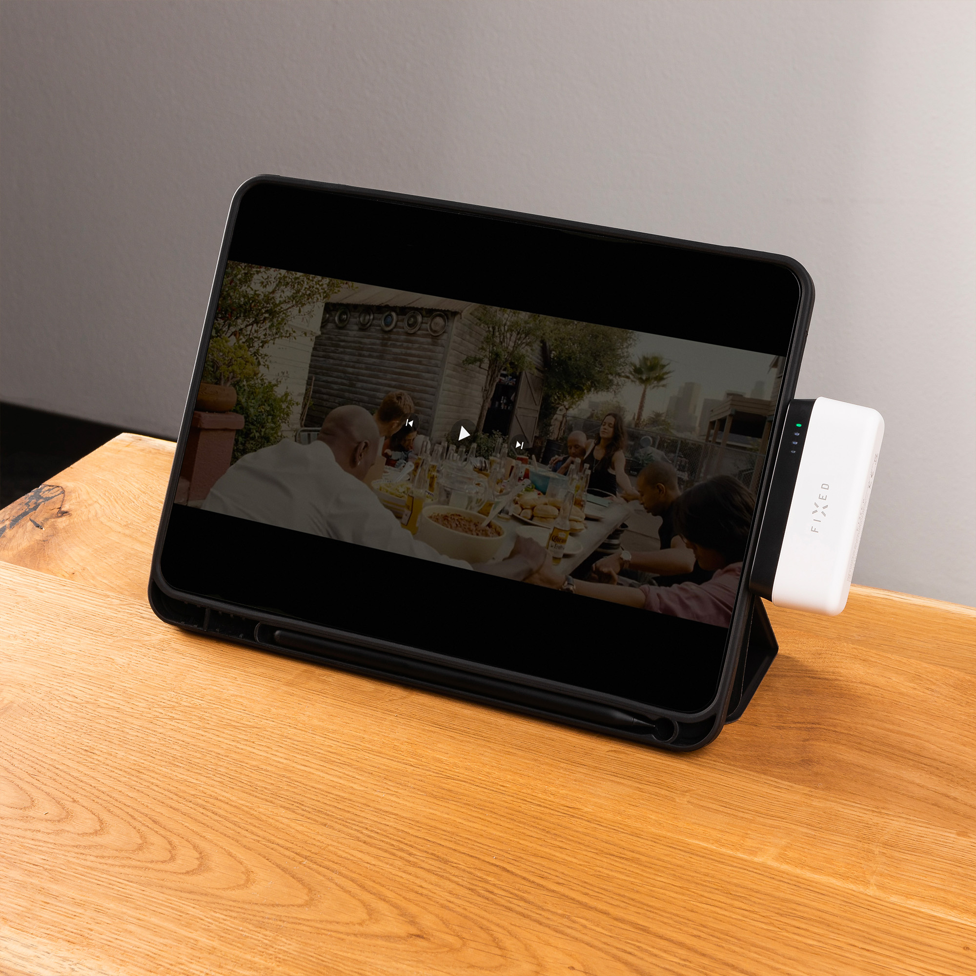 Tablet auf Holztisch zeigt Video von Personen beim Essen. Ein weißes Gerät ist mit dem Tablet verbunden.