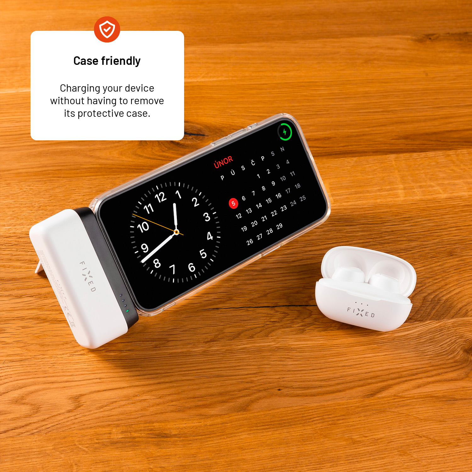 Eine Apple Watch und AirPods neben einem Ladegerät, alles auf einer Holzoberfläche. Die Uhr zeigt einen Kalender. Text: 'Case friendly'.
