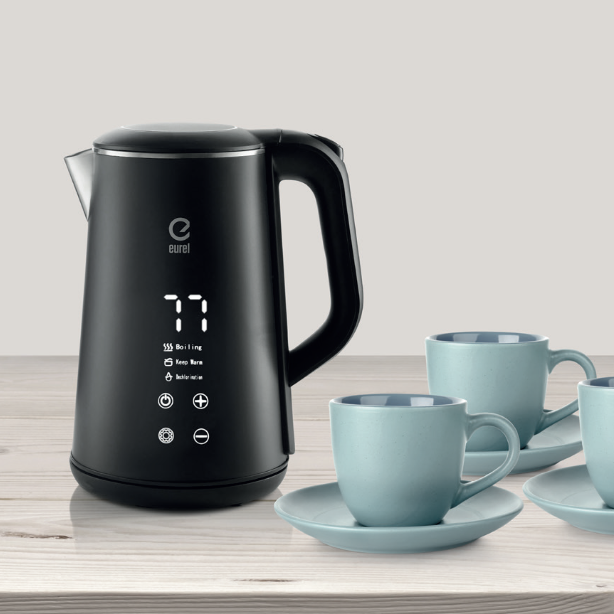 Ein schwarzer Wasserkocher mit Digitalanzeige und drei blaue Tassen und Untertassen auf einer Holzoberfläche.