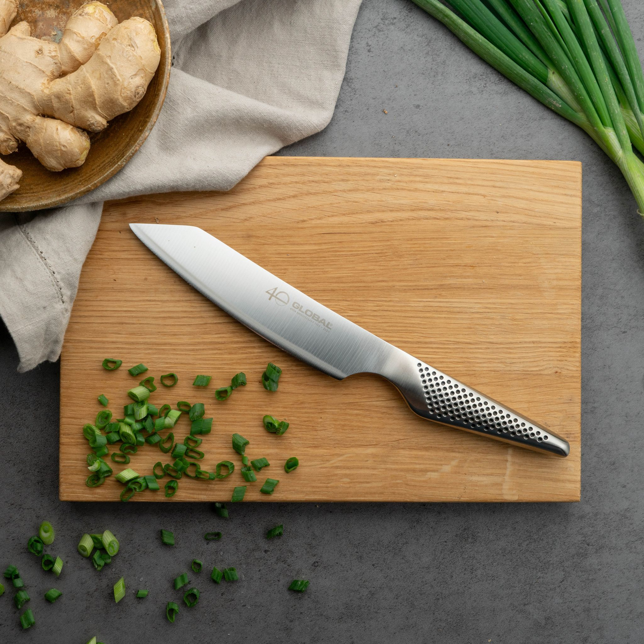 Ein Messer auf einem Holzbrett mit gehackten Frühlingszwiebeln. Ingwer in einer Schüssel und grüne Zwiebeln.