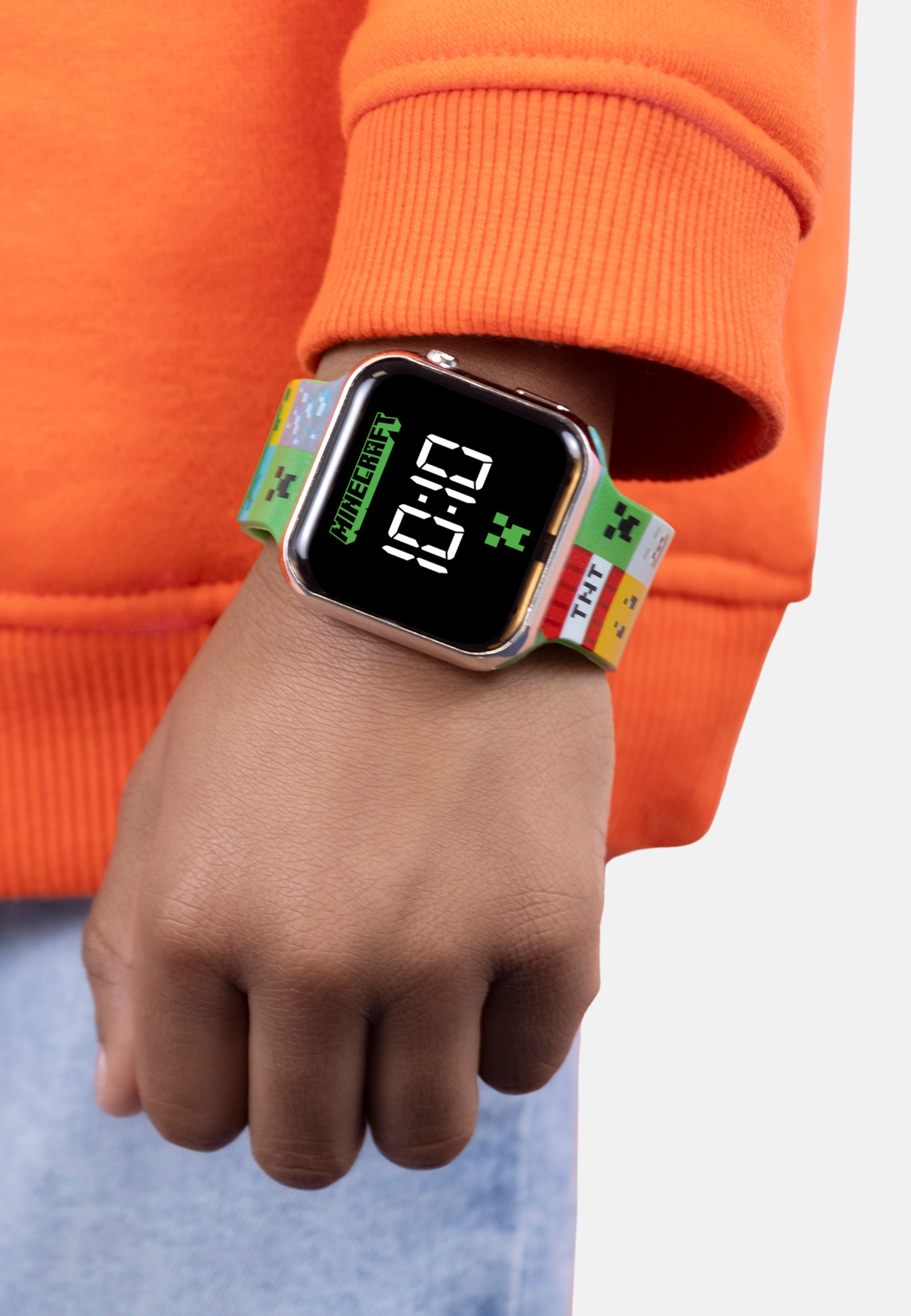 Am Handgelenk eines Kindes befindet sich eine Minecraft-Uhr mit digitaler Zeitanzeige. Die Uhr befindet sich an einem orangefarbenen Ärmel.
