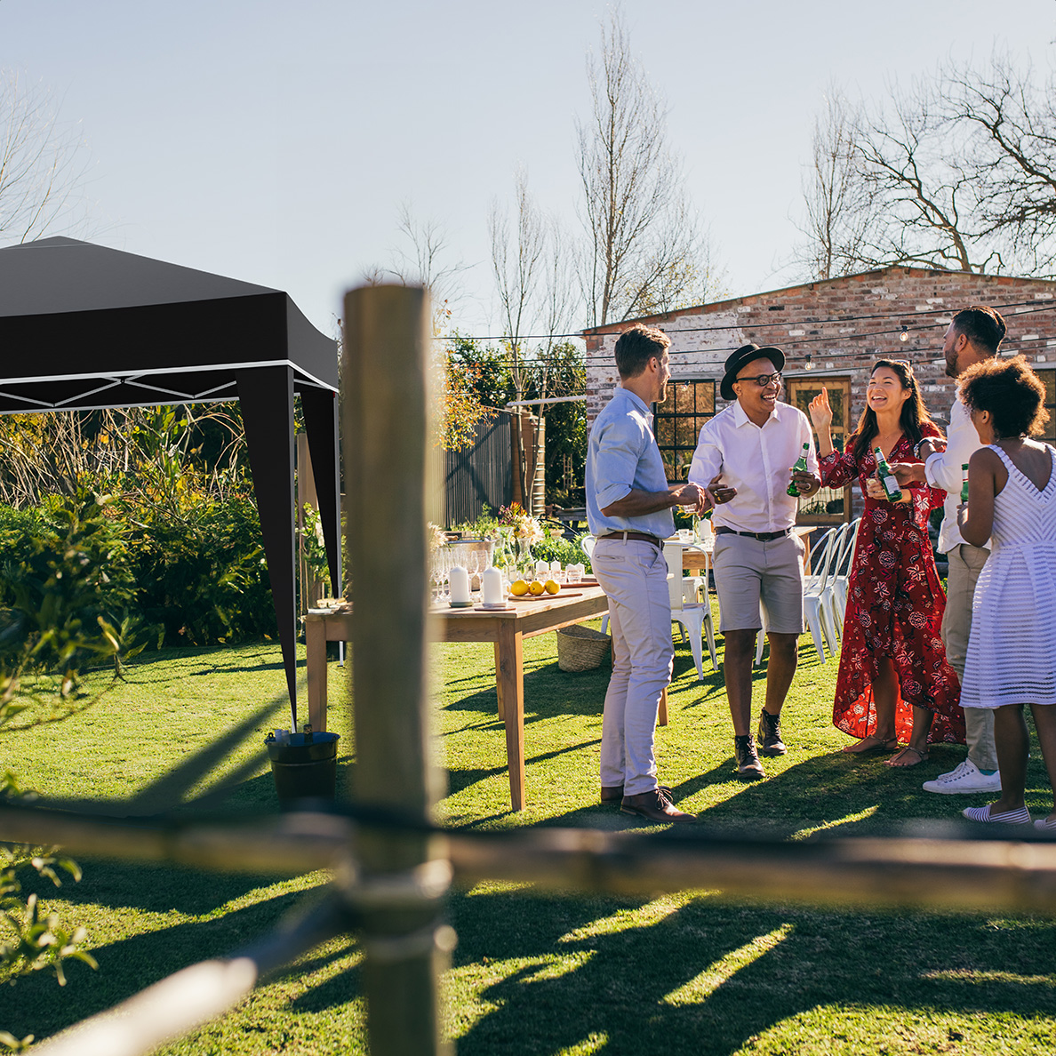 Groupe de personnes lors d'une fête dans le jardin. Ils boivent et discutent près d'une table et d'une tente noire par une journée ensoleillée.
