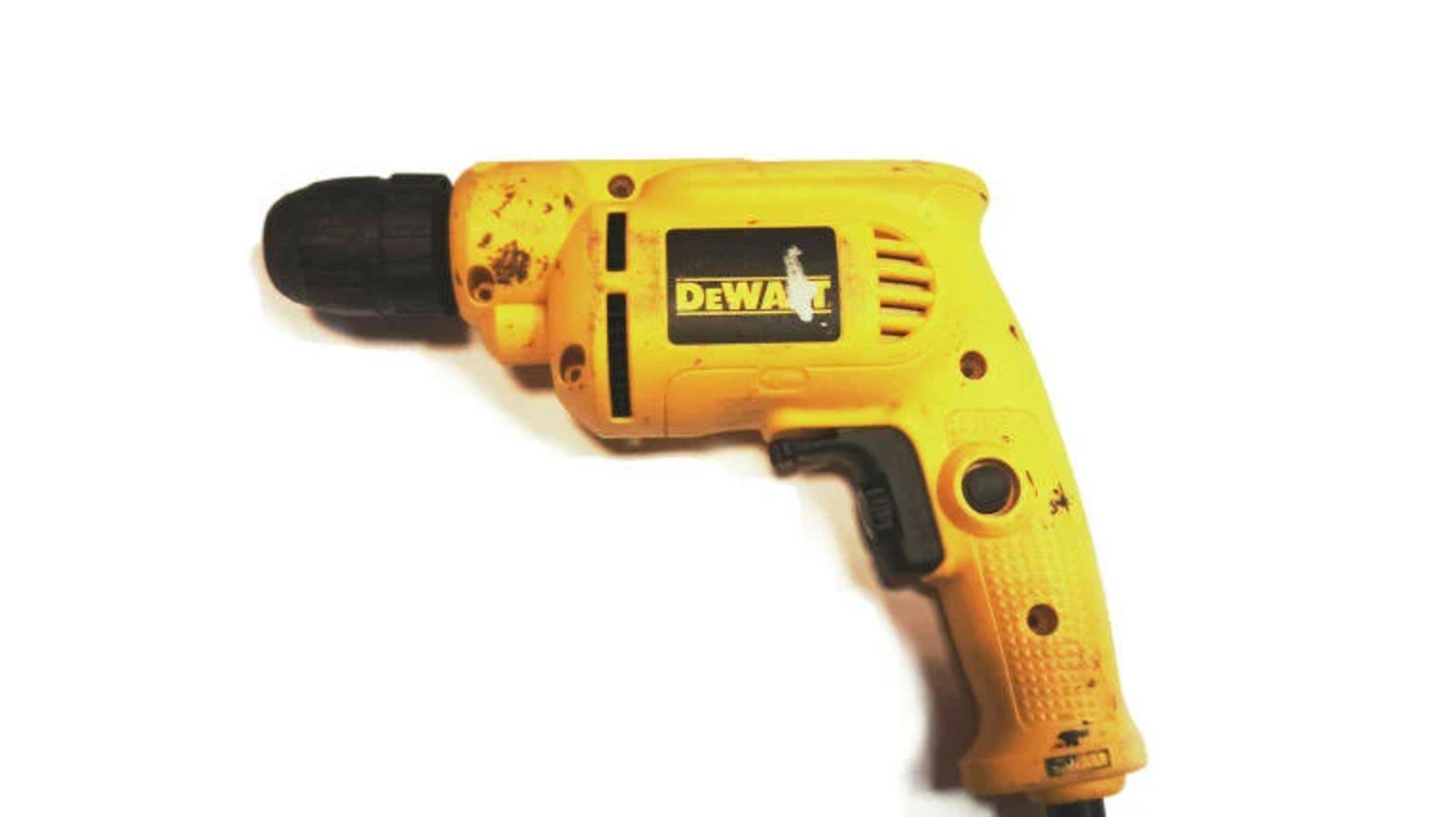 Sarı ve siyah bir DeWalt matkap beyaz bir yüzeyde duruyor. Matkap hafif aşınmış.