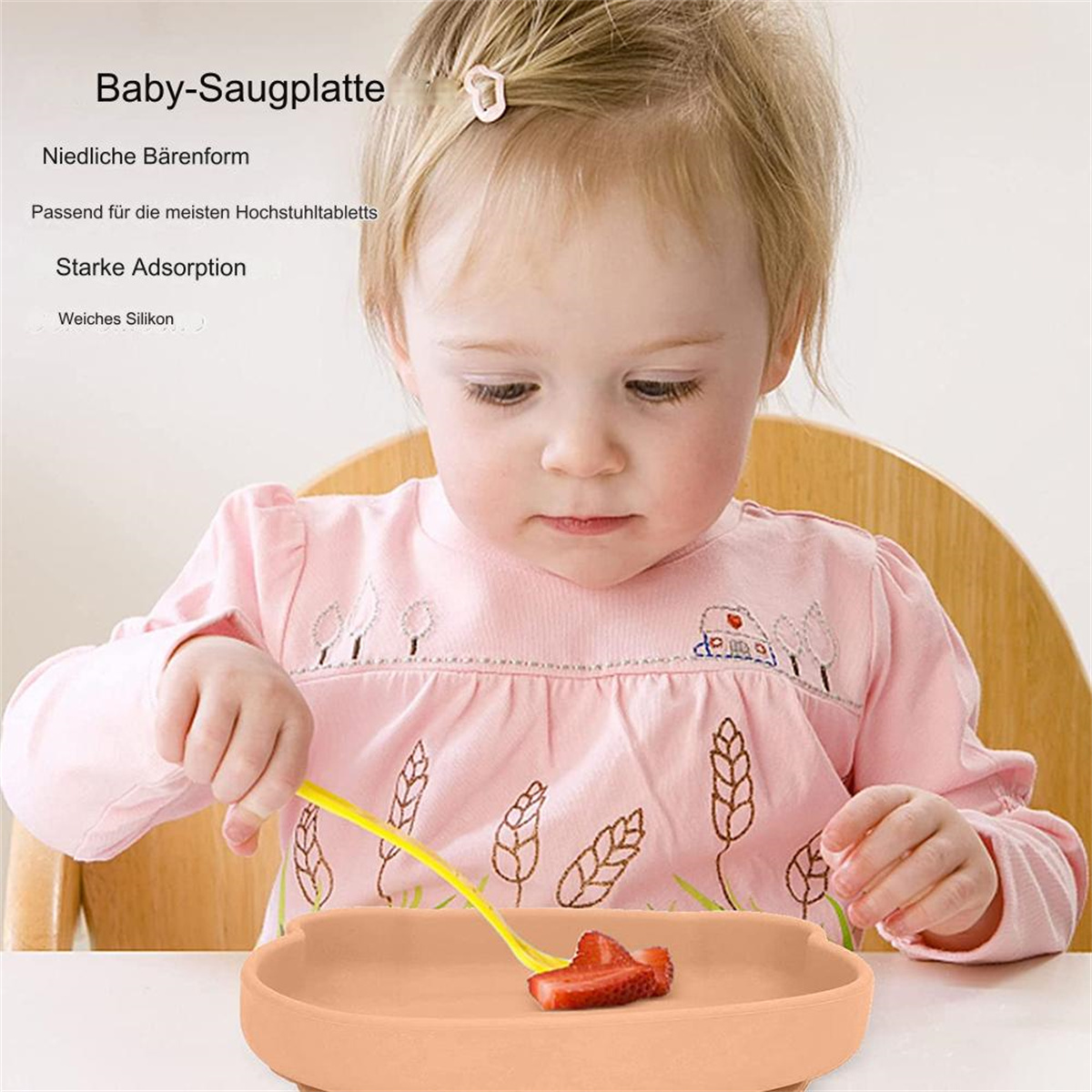 Ein Baby hält eine gelbe Gabel mit einem Erdbeerstück darauf. Das Baby sitzt vor einem orangefarbenen Saugteller.