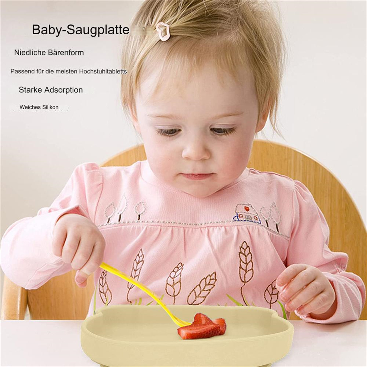 Ein Baby in rosa Hemd hält eine gelbe Gabel über einem beigefarbenen Teller mit einem Erdbeerstück. Das Baby sitzt in einem Hochstuhl.