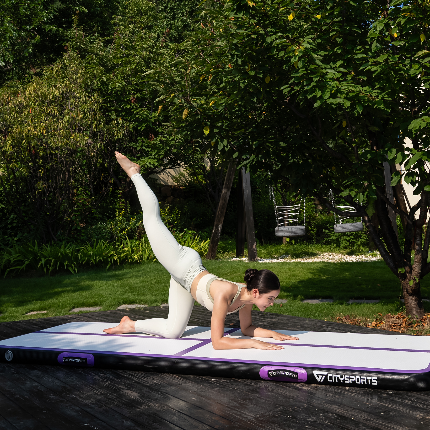 Woman doing yoga on a mat outdoors. She's in a plank position, leg extended. Green grass and trees surround her.