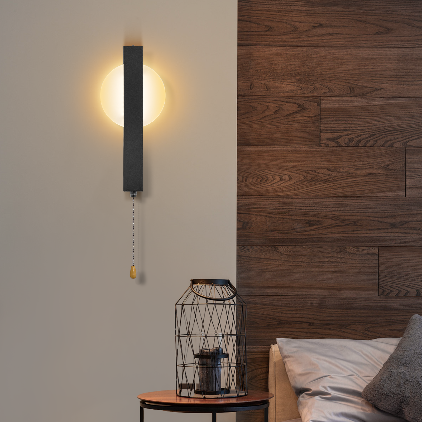 Una lampada da parete con catena è su un muro chiaro. Una gabbia decorativa e un letto sono sullo sfondo.