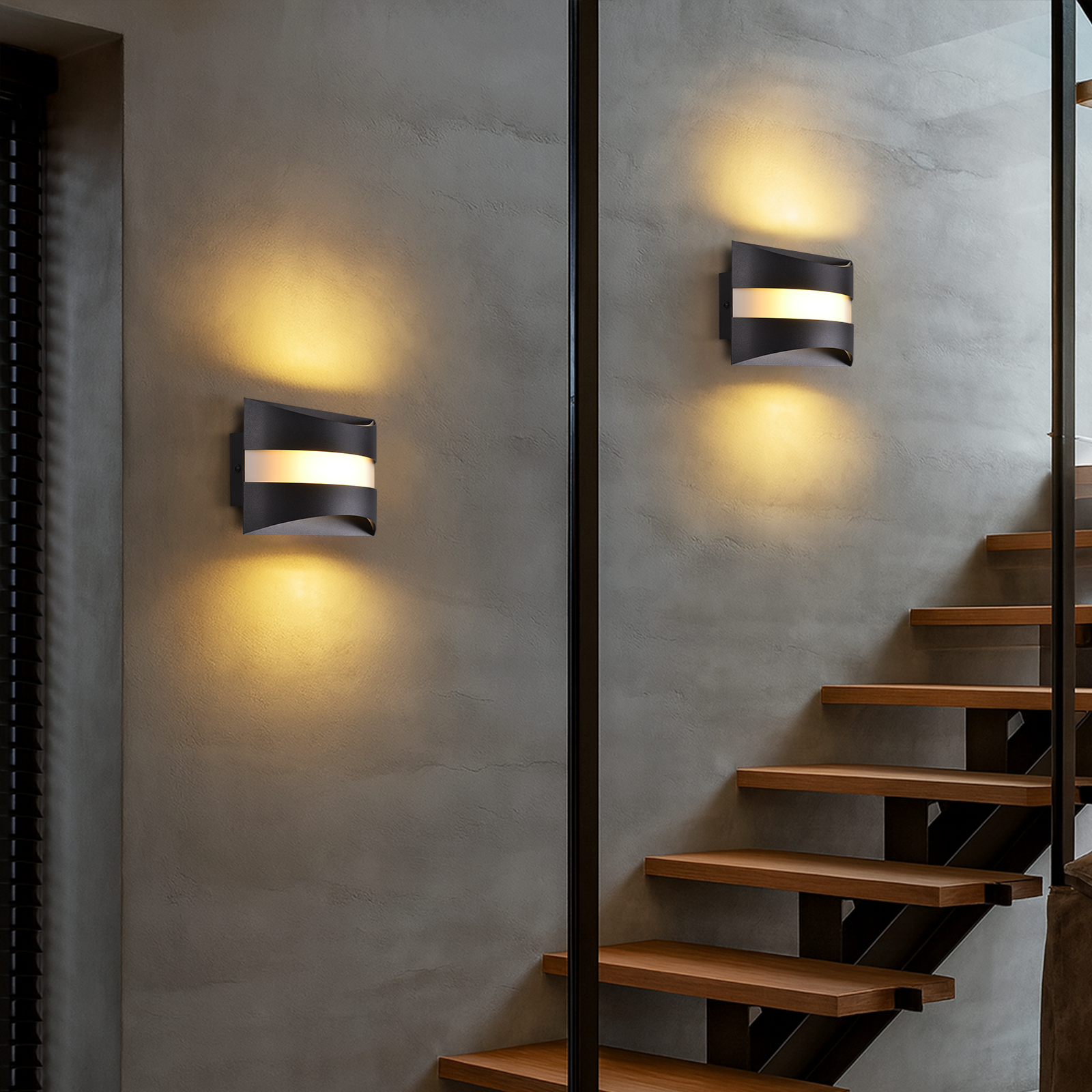 Due lampade da parete nere con luce intensa sono montate su un muro grigio. Scale in legno a destra.