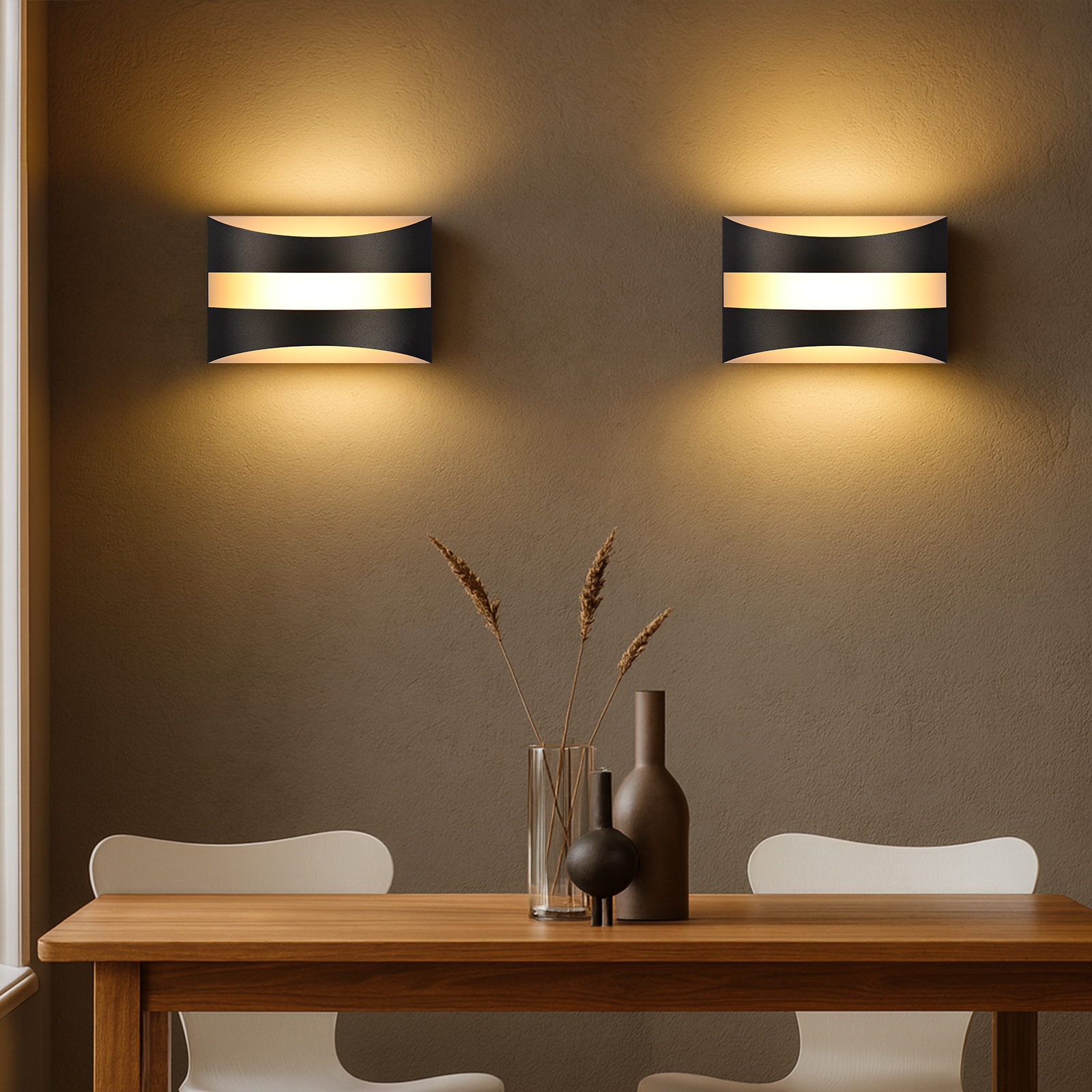 Due lampade da parete bianche e nere su un muro marrone, sopra un tavolo di legno con decorazioni e due sedie.