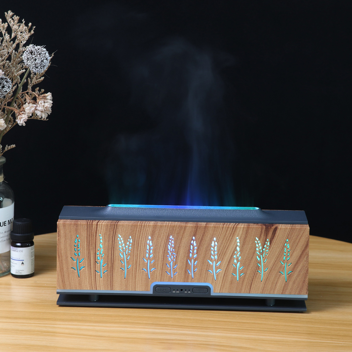 Aroma-Diffusor aus Holz mit Dampf und blauem Licht. Trockenblumen und eine Flasche ätherisches Öl stehen auf einem Holztisch. Schwarzer Hintergrund.