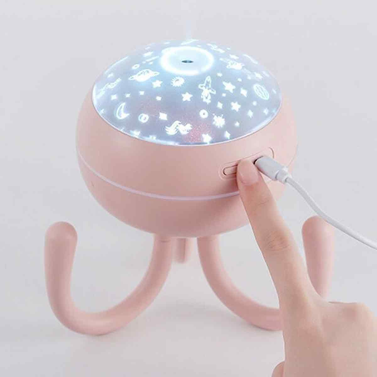 Ein rosa Sternenprojektor, an den eine Hand ein USB-Kabel anschließt. Der Projektor befindet sich auf weißem Hintergrund und zeigt Sterne.