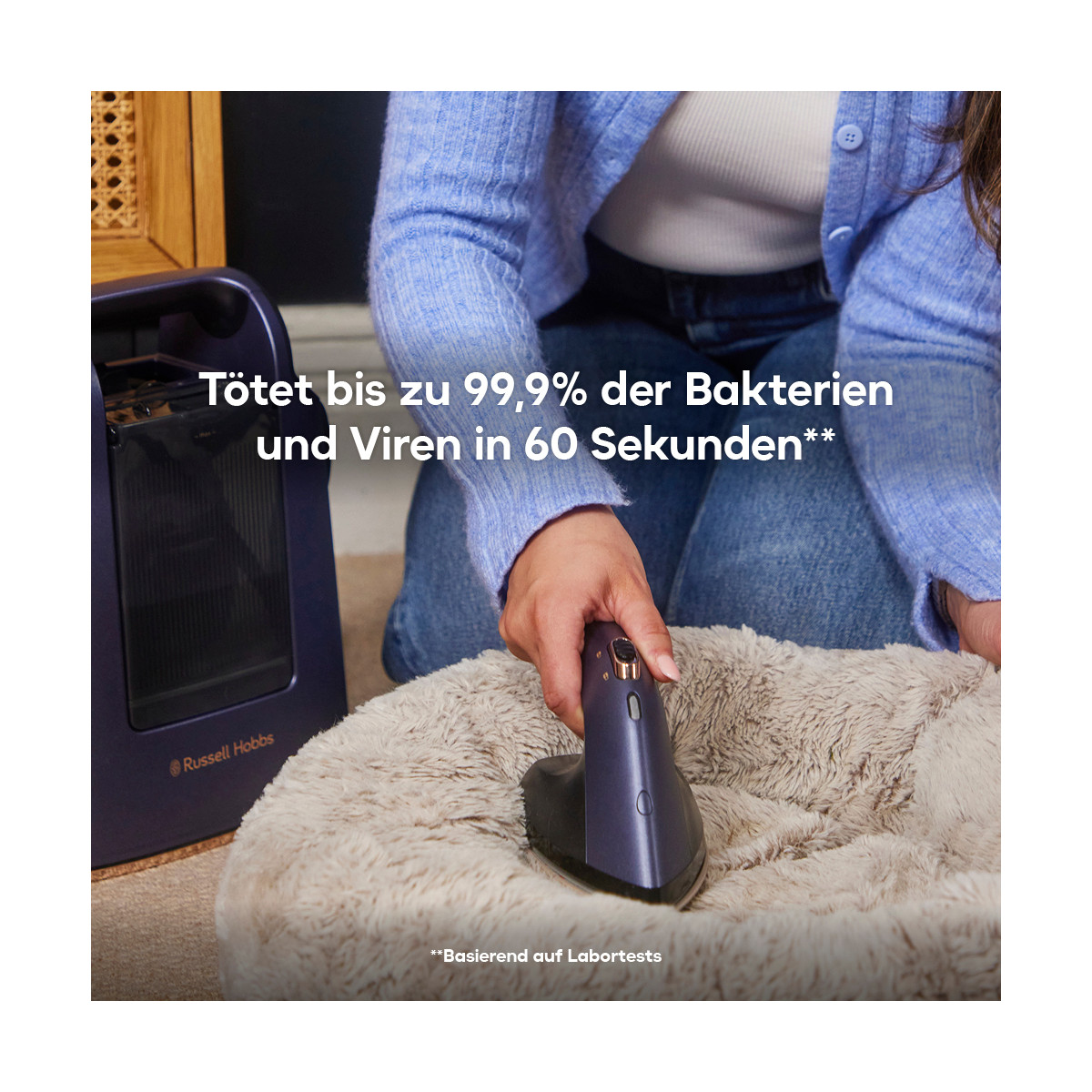 Une personne utilise un appareil de nettoyage sur un lit pour animaux de compagnie. Un appareil violet est tenu au-dessus du lit moelleux. Une machine est visible en arrière-plan.