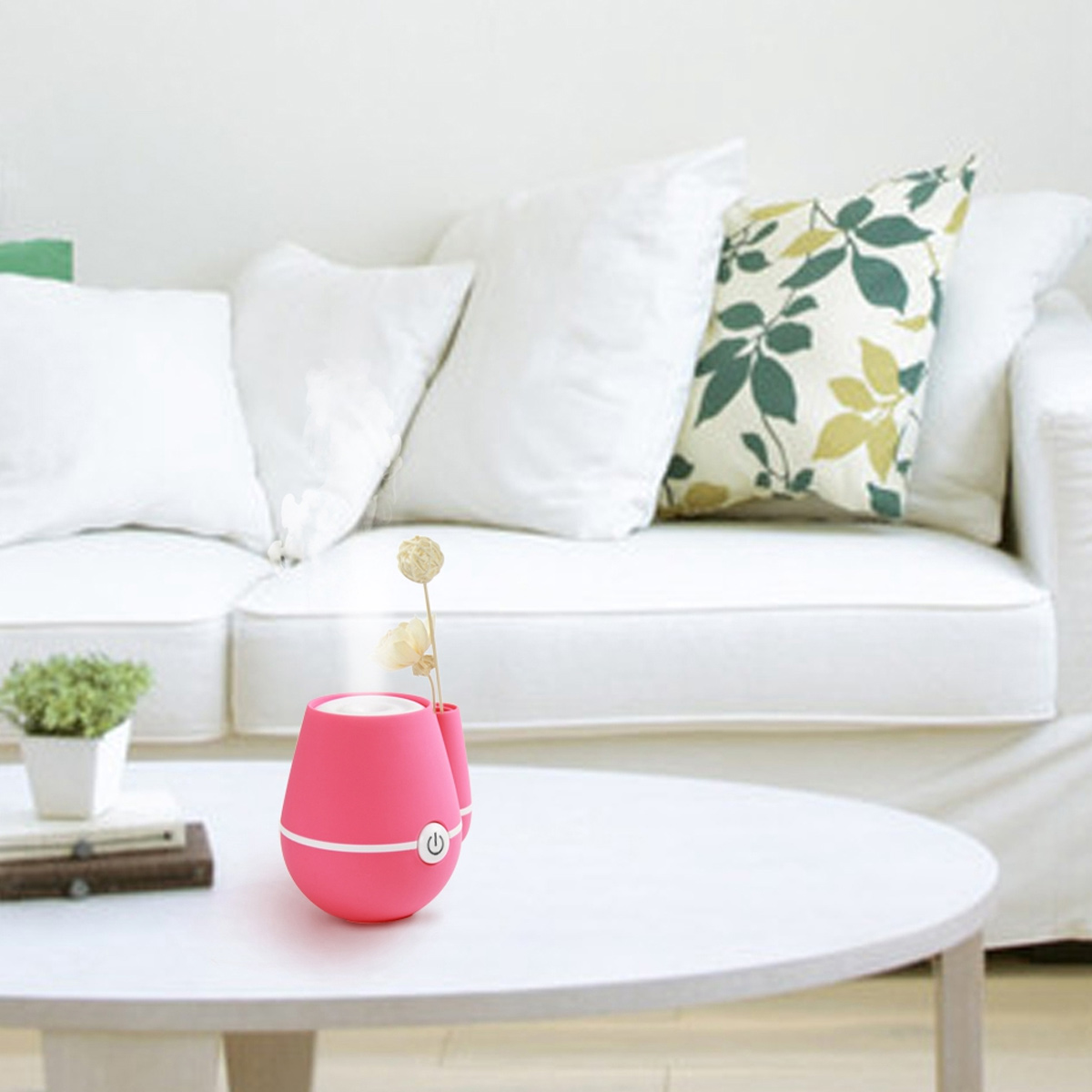 Ein rosa Diffusor für ätherische Öle auf einem weißen Tisch. Weißes Sofa und Kissen im Hintergrund. Trockenblumen im Diffusor.