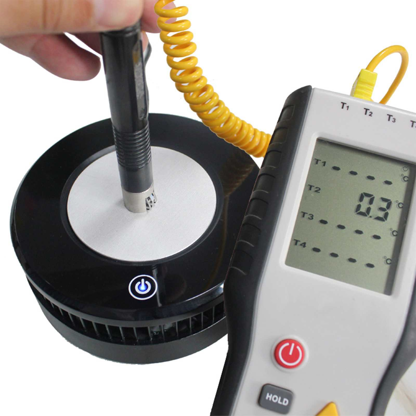 Eine Hand hält eine Sonde über einem schwarzen Gerät mit weißer Mitte. Ein digitales Thermometer zeigt 0,3 °C an. Ein gelbes Kabel verbindet sie.