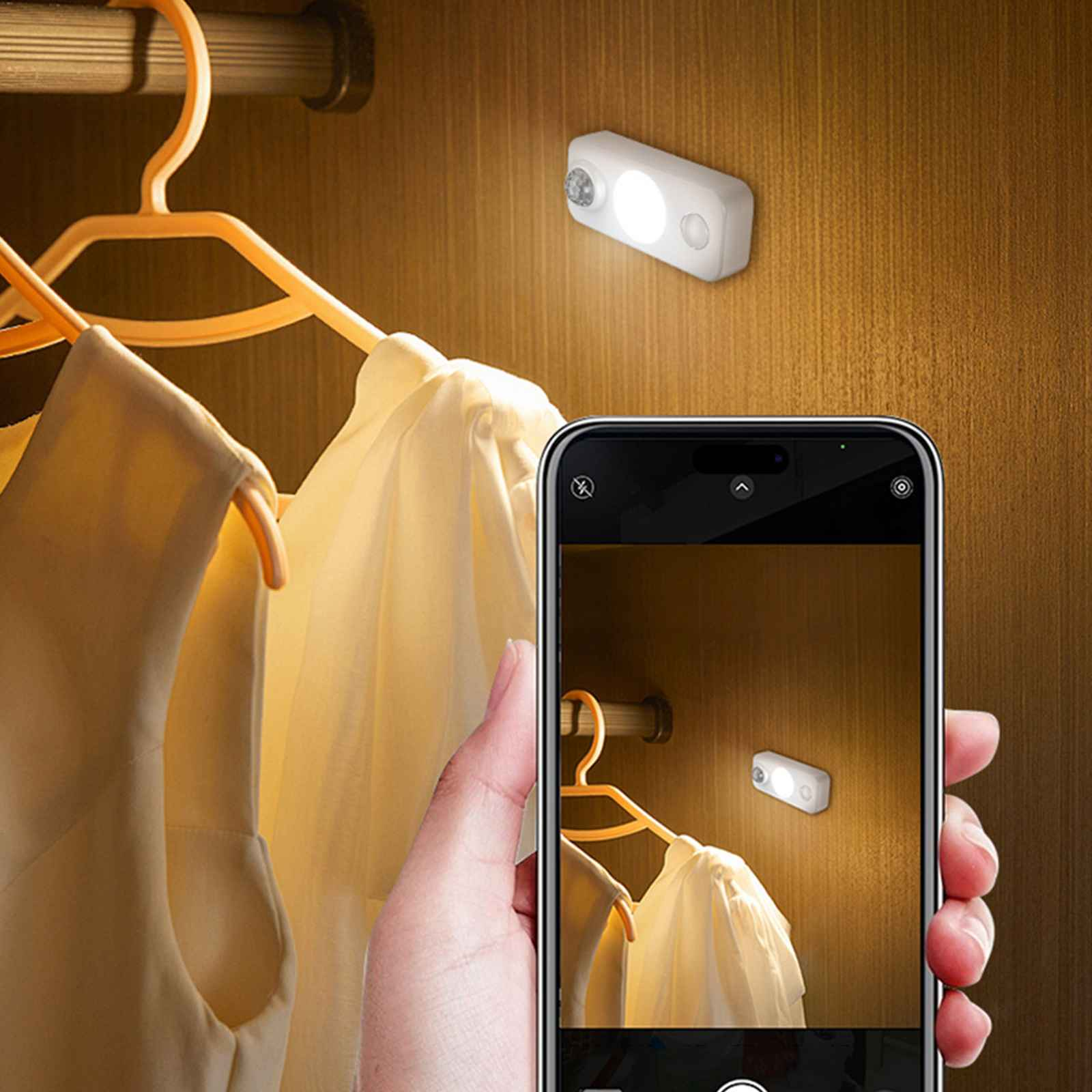 Eine Hand, die ein Telefon hält und ein Foto von einer Schrankleuchte macht. Kleidung auf Kleiderbügeln ist im Hintergrund sichtbar.
